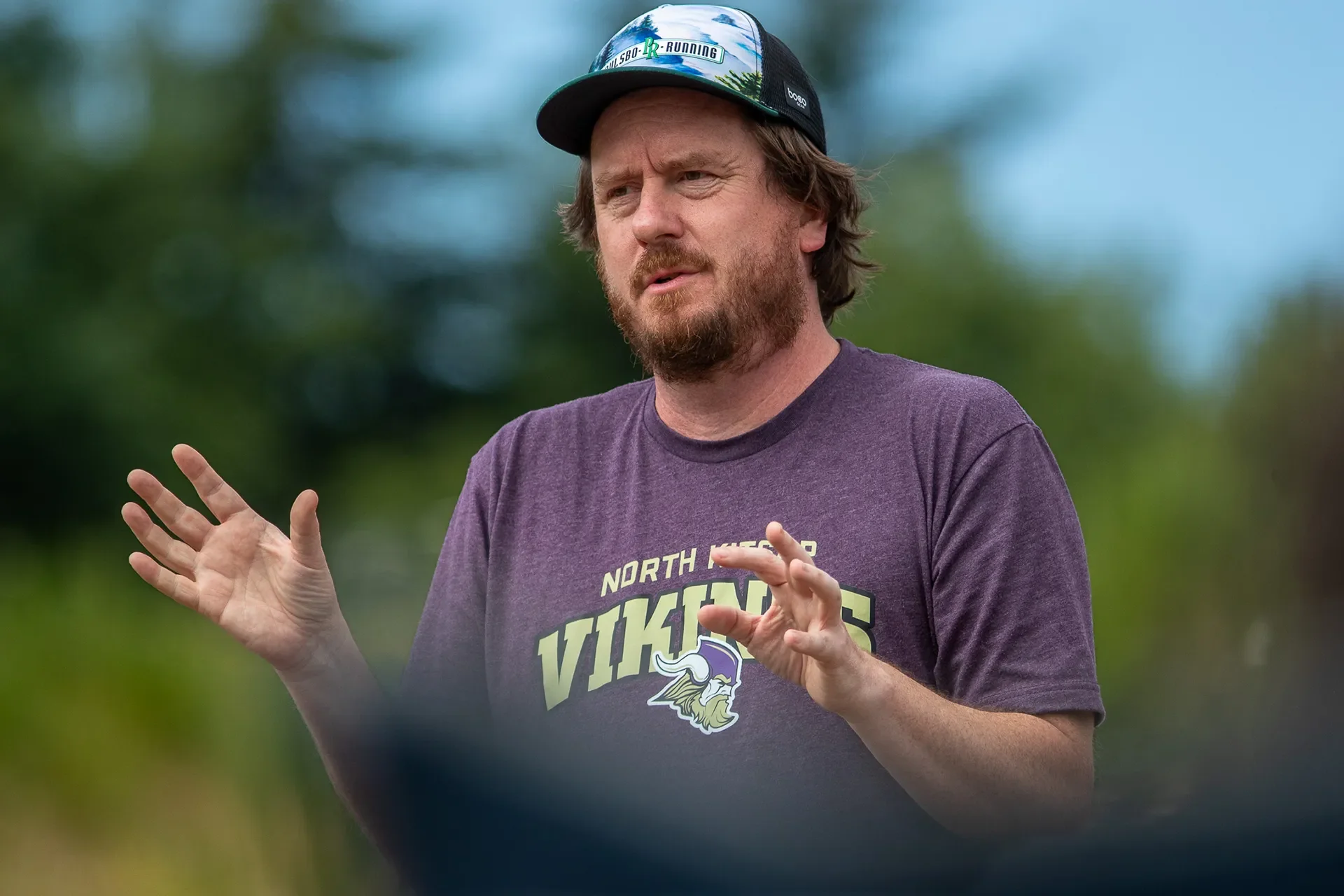 Coach Jonathan Erickson standing outdoors talking to athletes about running shoe fitment.