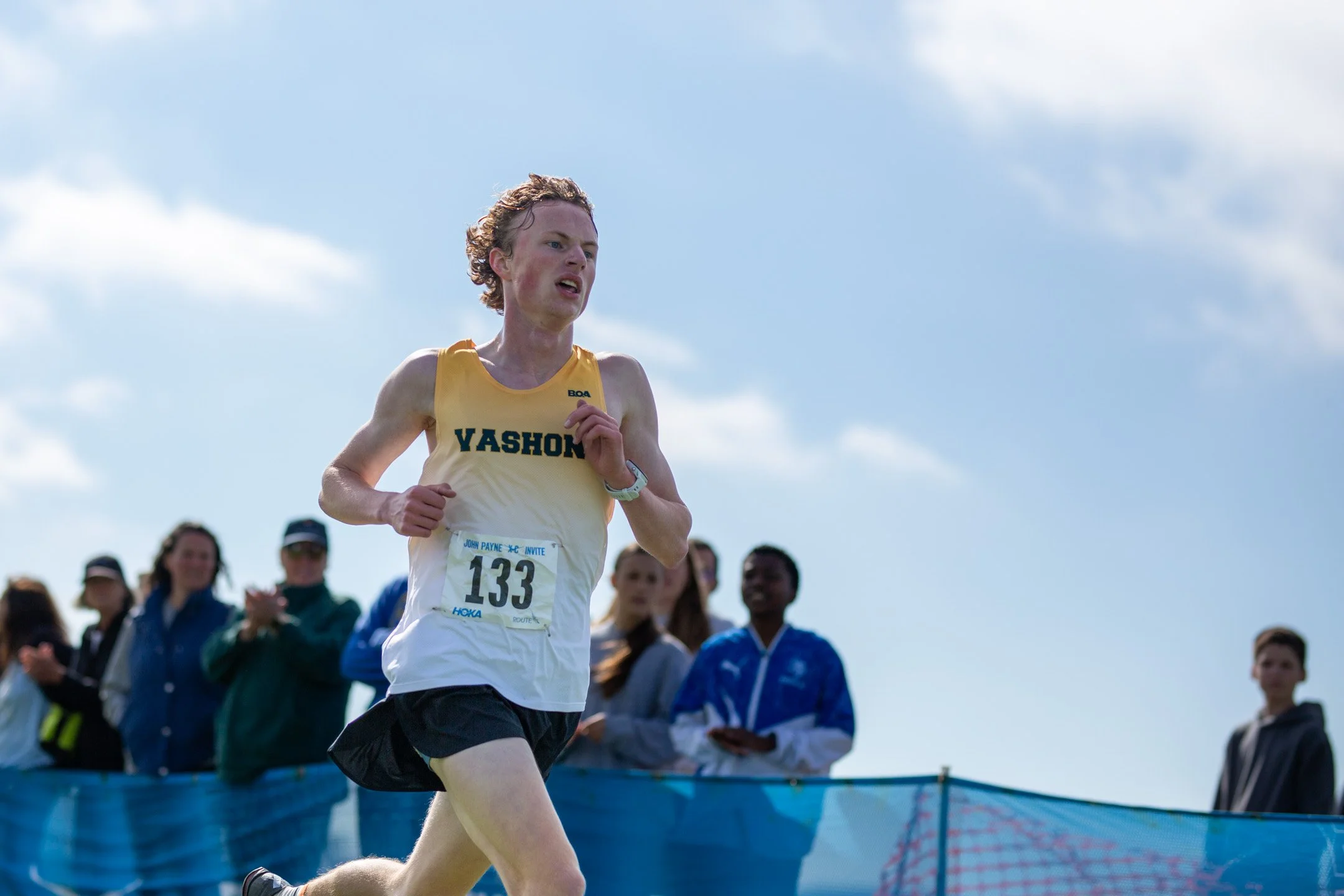 Vashon Island senior Joshua Healey in a yellow singlet with bib 133 running solo toward the finish line against an open sky.