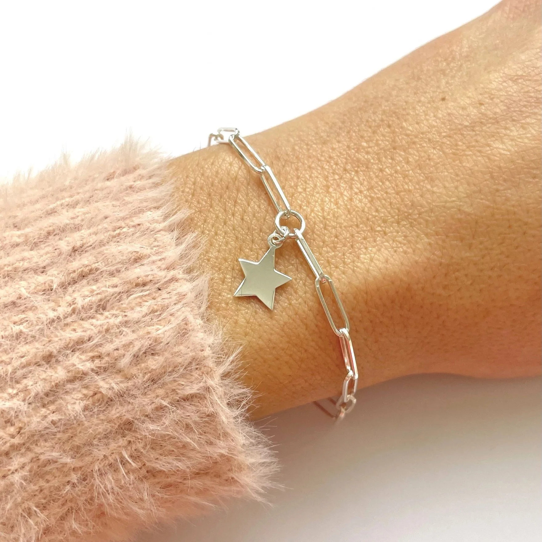 A silver bracelet with a star-shaped charm worn on a person's wrist, with a pink fuzzy sleeve visible.