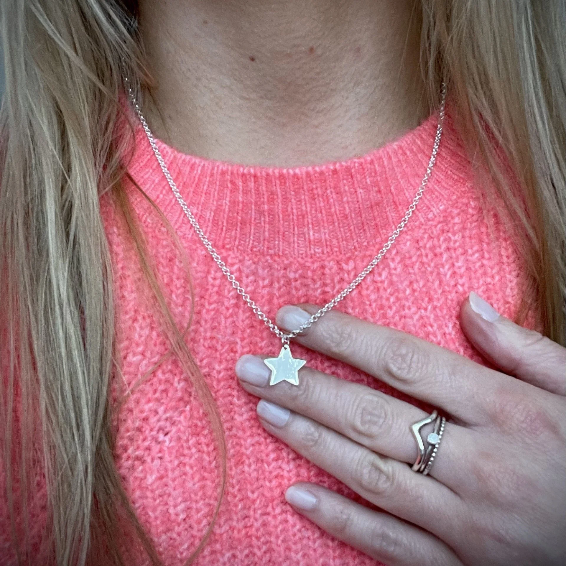 A woman wearing a pink knit sweater, a star-shaped pendant necklace, and a ring with a star design on her finger.