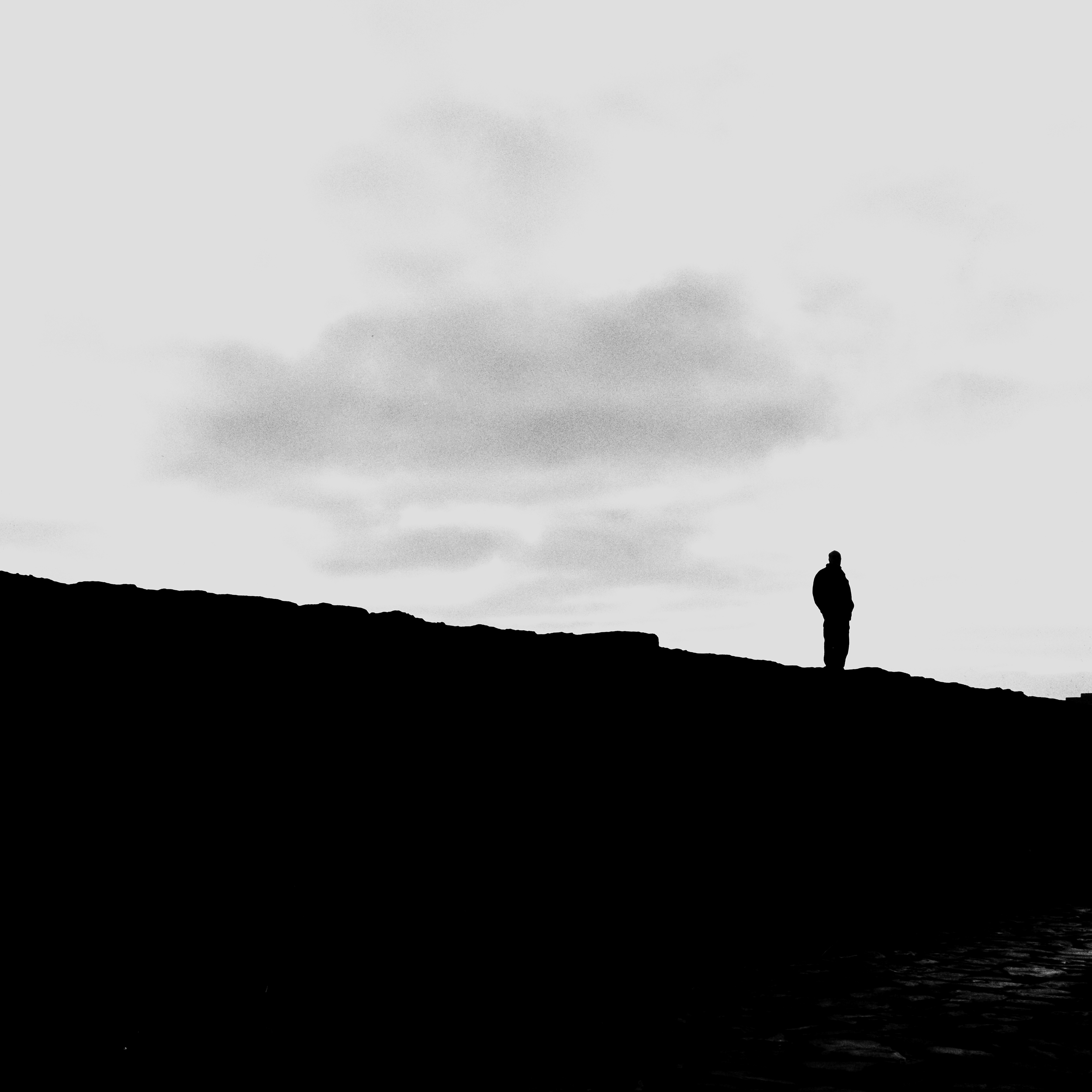 Silhouette of a person standing on a hill against a cloudy sky.