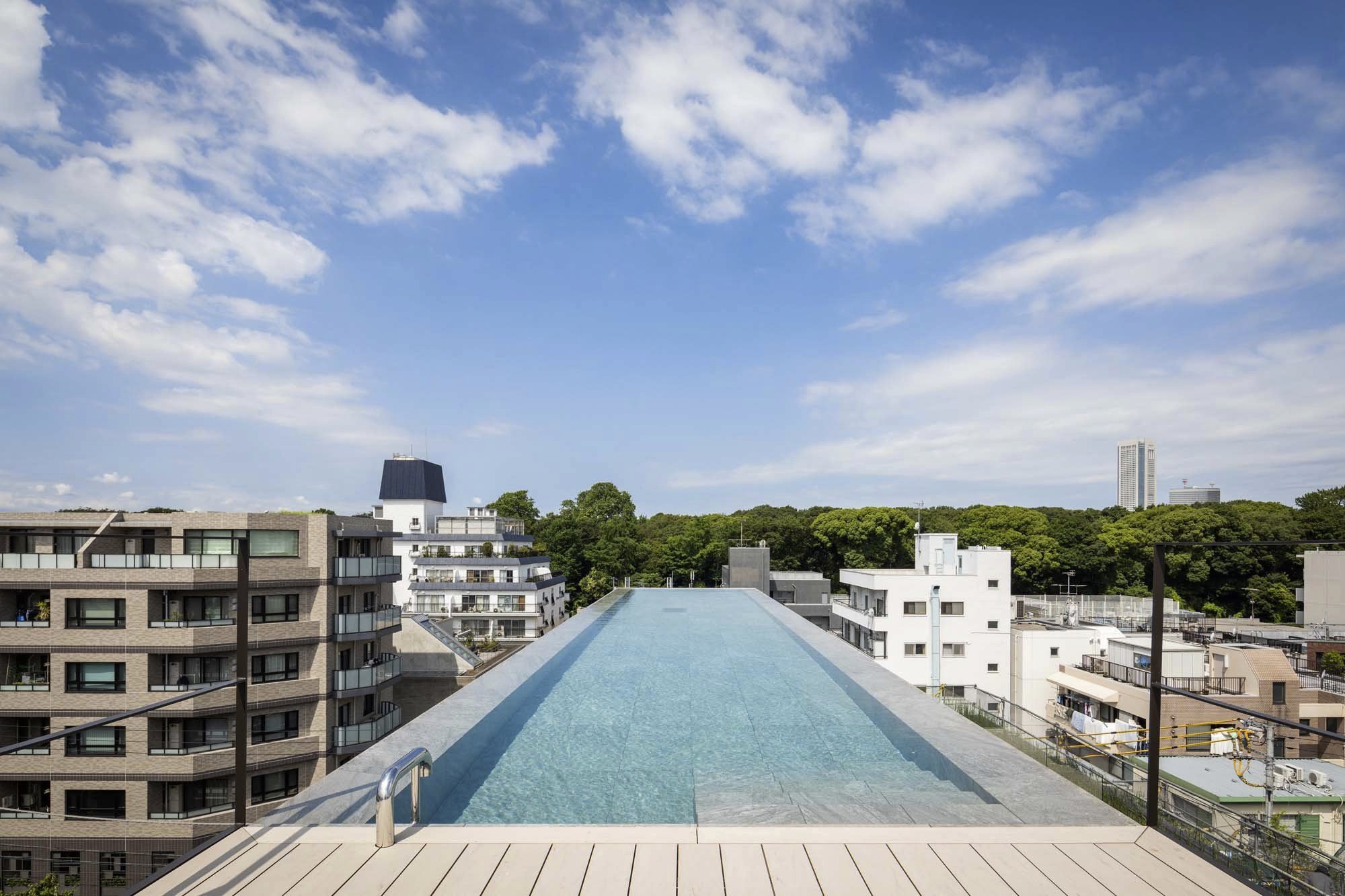 Kengo Kuma and Associates - The Kita - Westbank Corp. - Tokyo - Modern building with brown vertical lines, large windows, surrounded by green trees, city background.2
