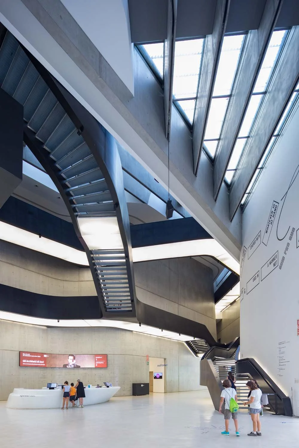 Zaha Hadid - Maxxi Museum - The image shows a modern architectural interior with a staircase, information desk, and wall diagram.