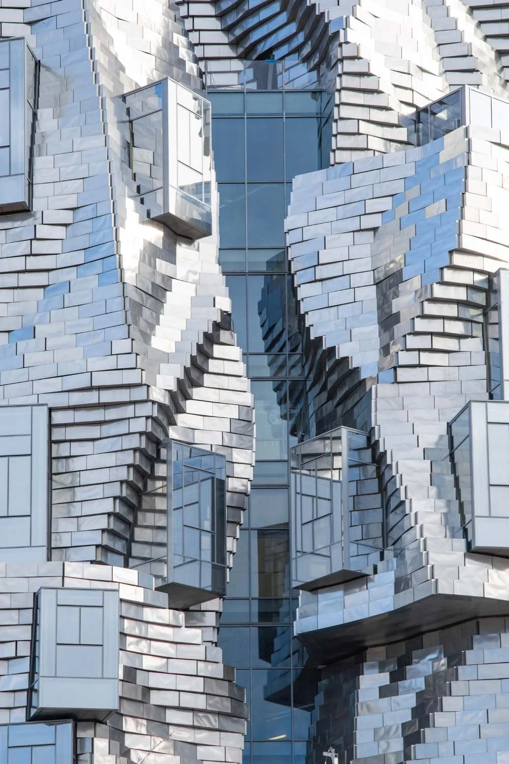 Close-up view of a modern building with a geometric facade made of white bricks and glass windows, featuring a textured, layered design.