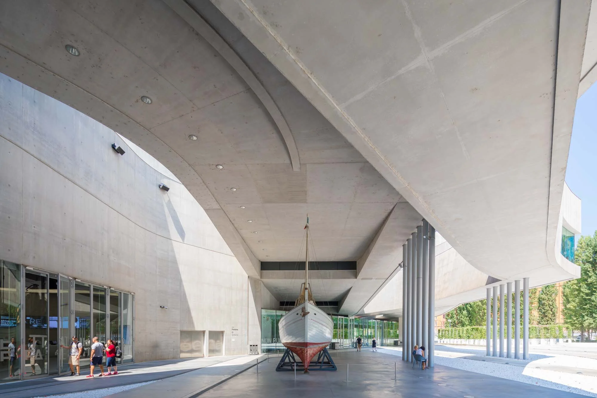 Zaha Hadid - Maxxi Museum - Modern architectural structure houses a white boat; people explore the spacious, well-lit area with tall columns and shadows