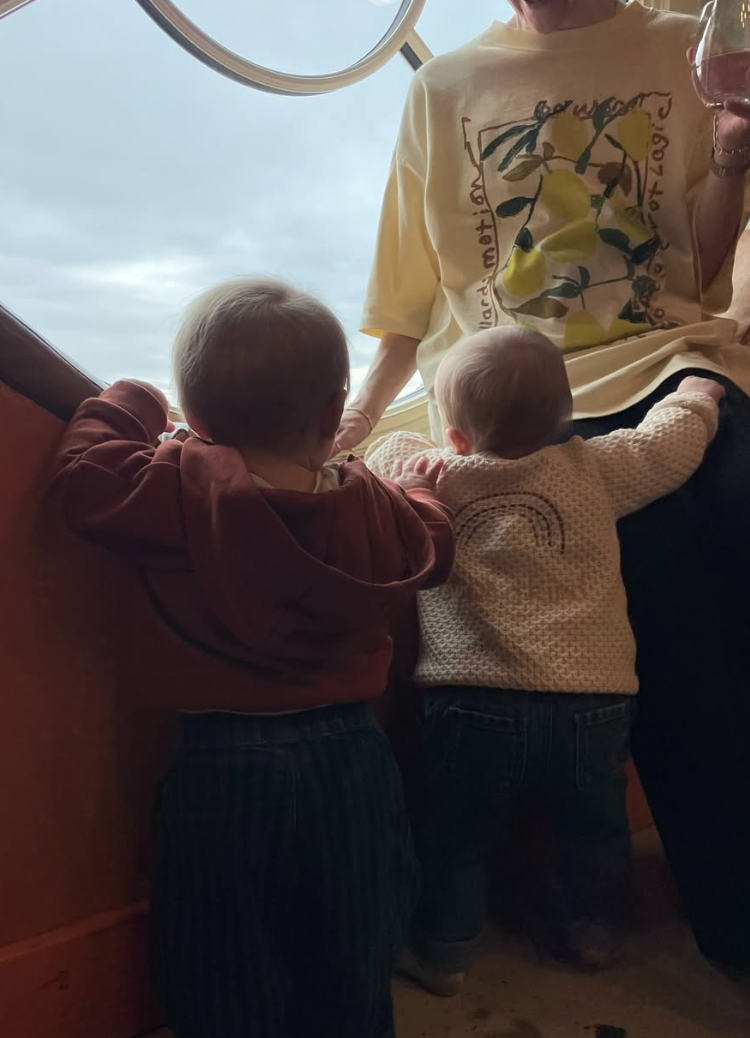 Two young children and an adult looking out of a large circular window, with cloudy sky visible outside.