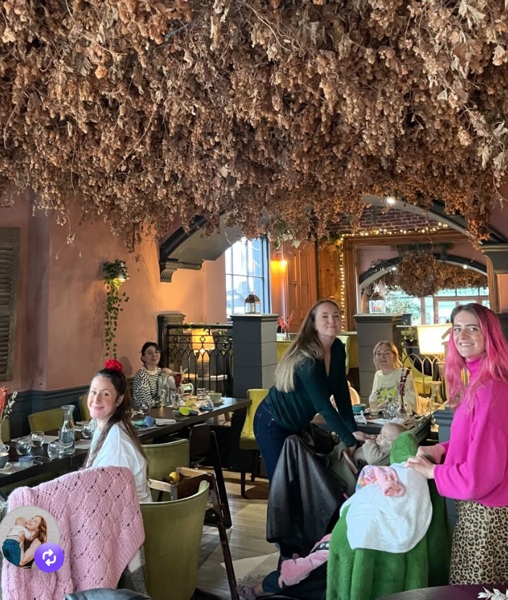Group of women gathered in a restaurant with a decorated ceiling of hanging dried flowers or foliage, enjoying a meal and drinks.