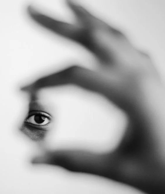 A person peering through a small circular opening, with their eye clearly visible and hand framing the view.