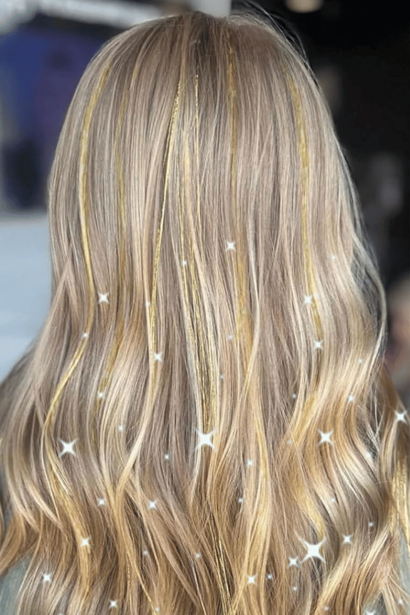 Blonde hair with subtle waves and thin golden fairy hair tinsel in her hair.
