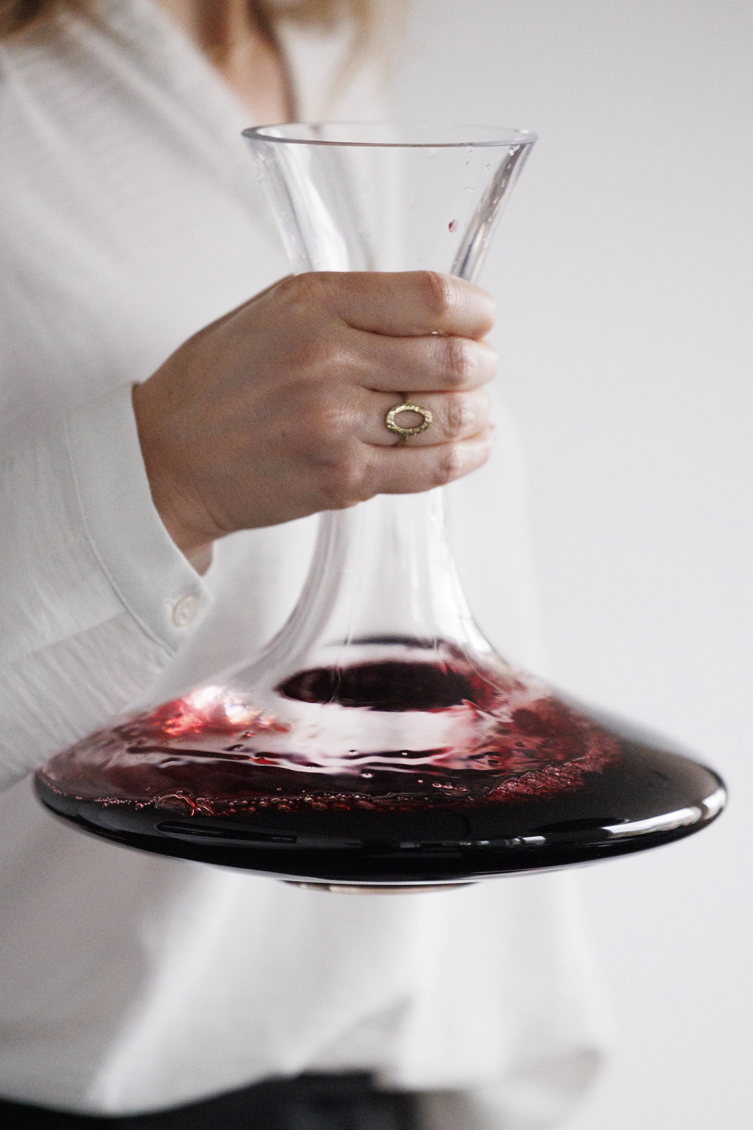 Hand met een ring, houd een karaf met rode wijn.