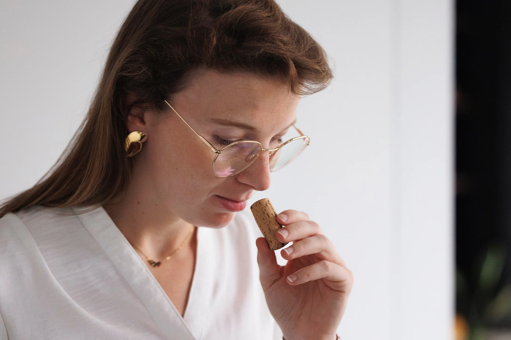 Vrouw met bril en oorbellen ruikt een wijnstopper.