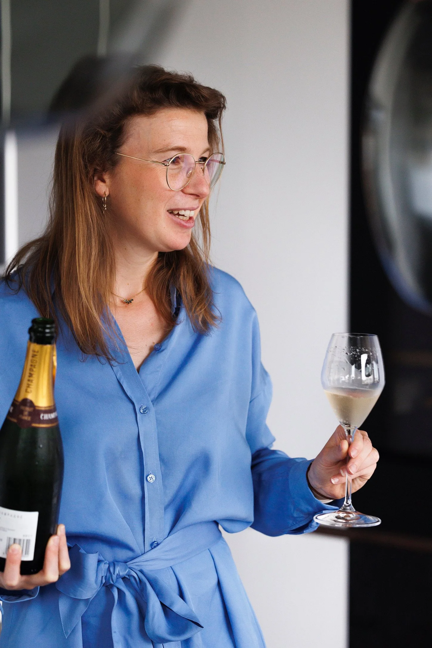 Vrouw in een blauwe blouse houdt een glas wijn en een fles champagne.