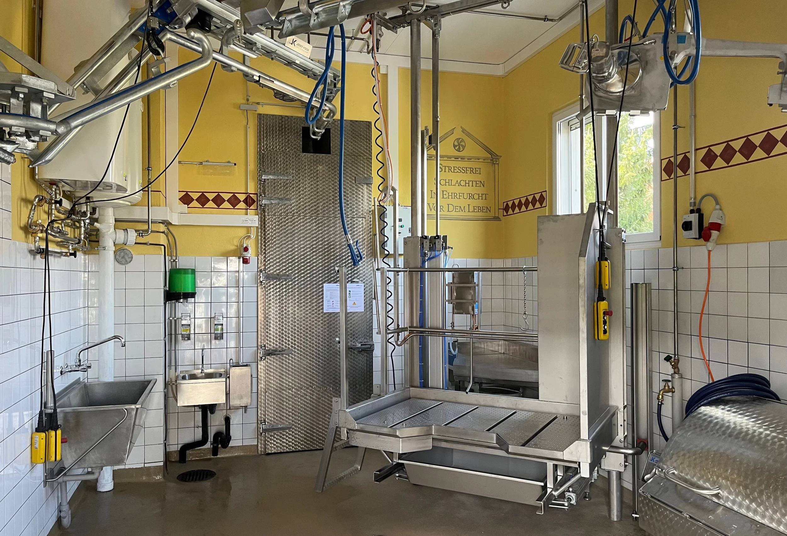 Reinigungs- und Desinfektionsraum mit Edelstahl- und Fliesenspiegeln, Wasserbecken, Rohrleitungen, Steuerungen und Fenster.