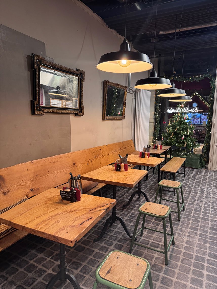Innenaufnahme eines cafés mit Holztischen, grünen Hockern, einer Weihnachtsbaumdekoration und modernen schwarzen Hängelampen.
