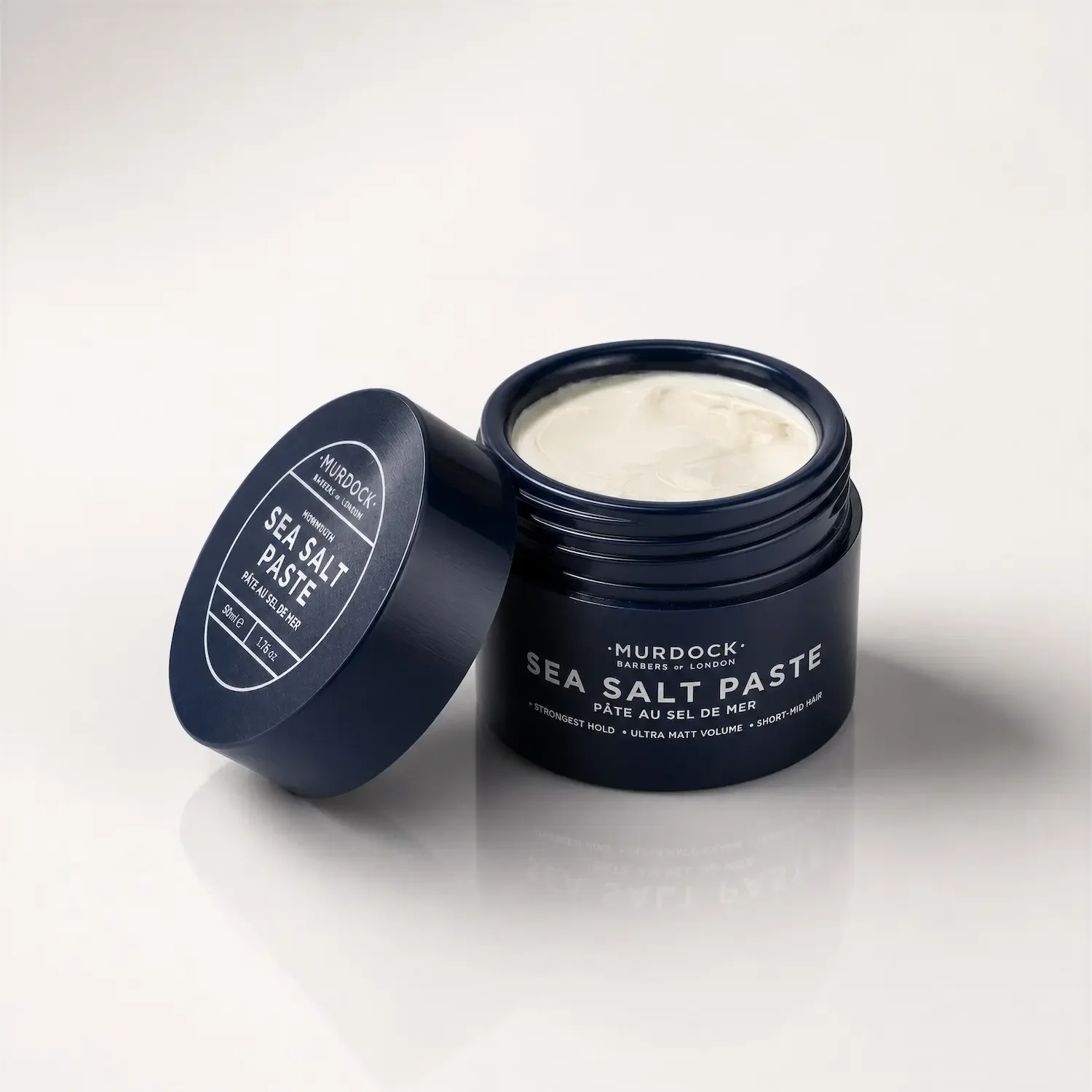 A black jar of Murdock Sea Salt Paste with a partially open lid, revealing a white, creamy product inside, set against a white background.
