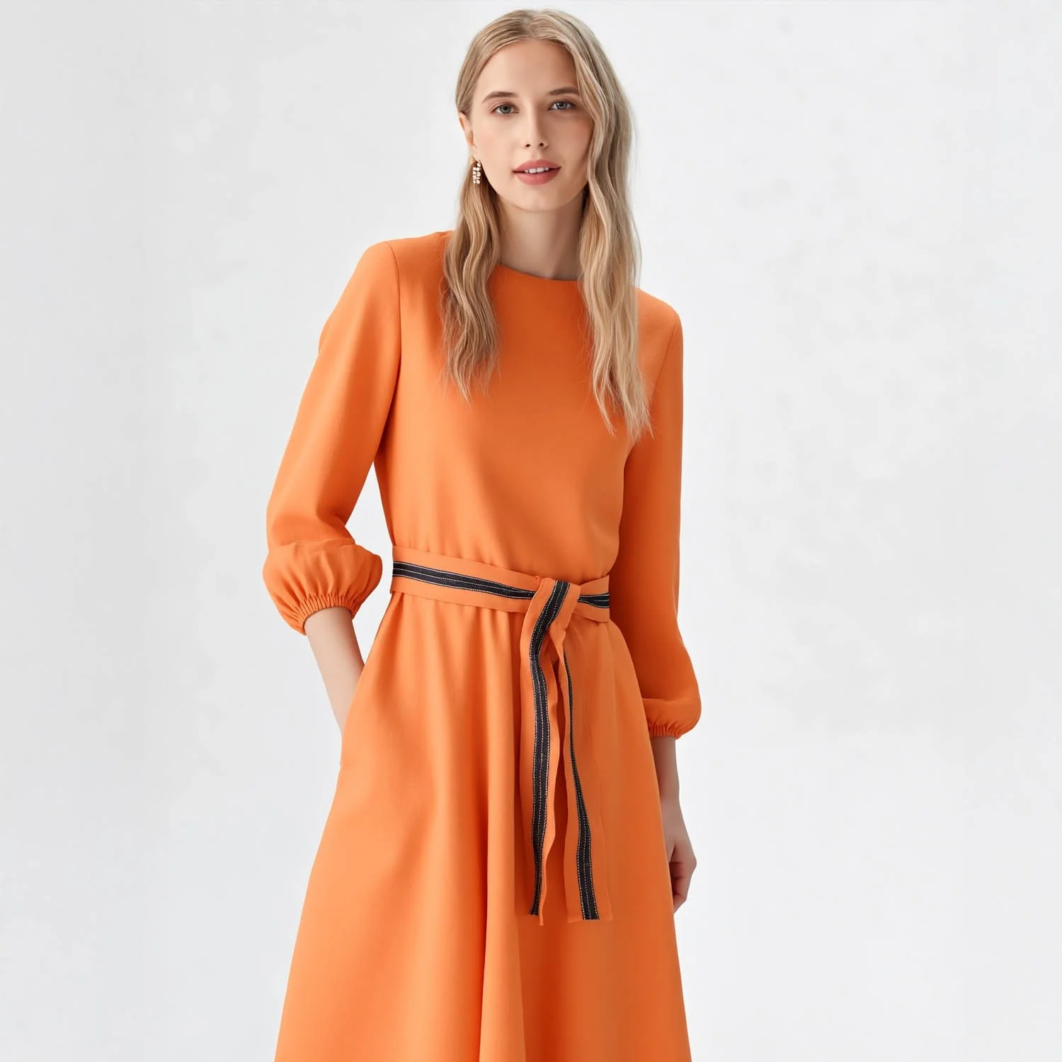 A virtual on model woman with long blonde hair wearing an orange dress with three-quarter sleeves and a black-and-orange striped belt.