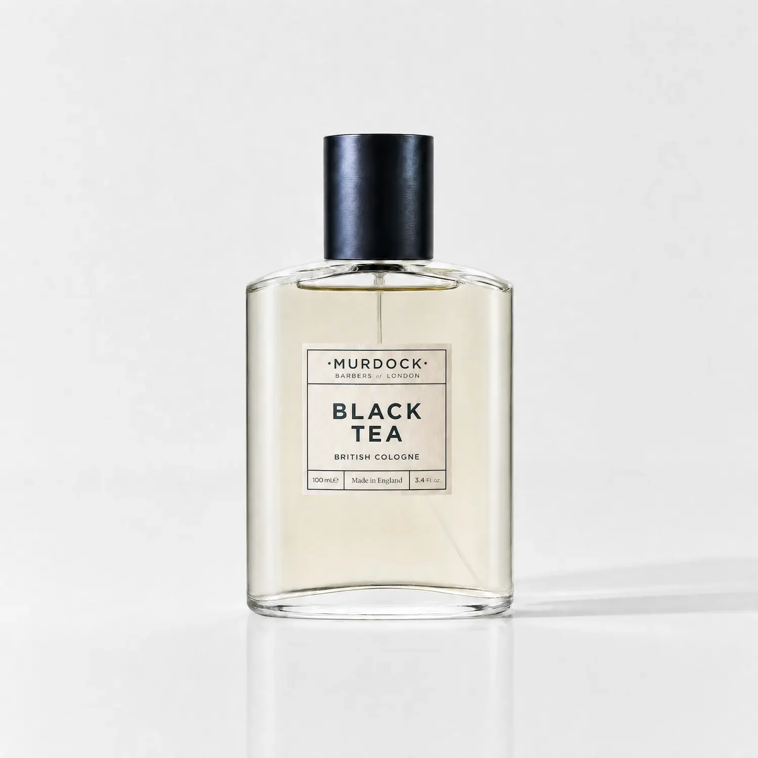 A clear glass bottle of Murdock Black Tea British Cologne with a black cap, standing upright against a gray background.