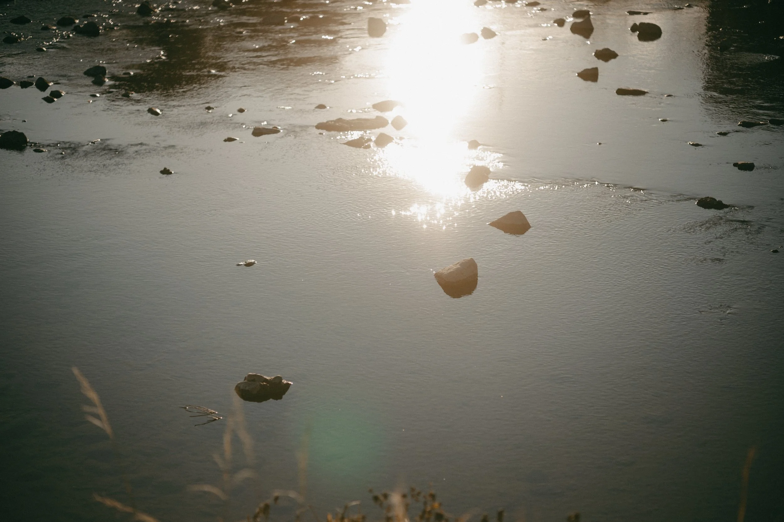 Sun reflecting on a calm body of water with scattered rocks.