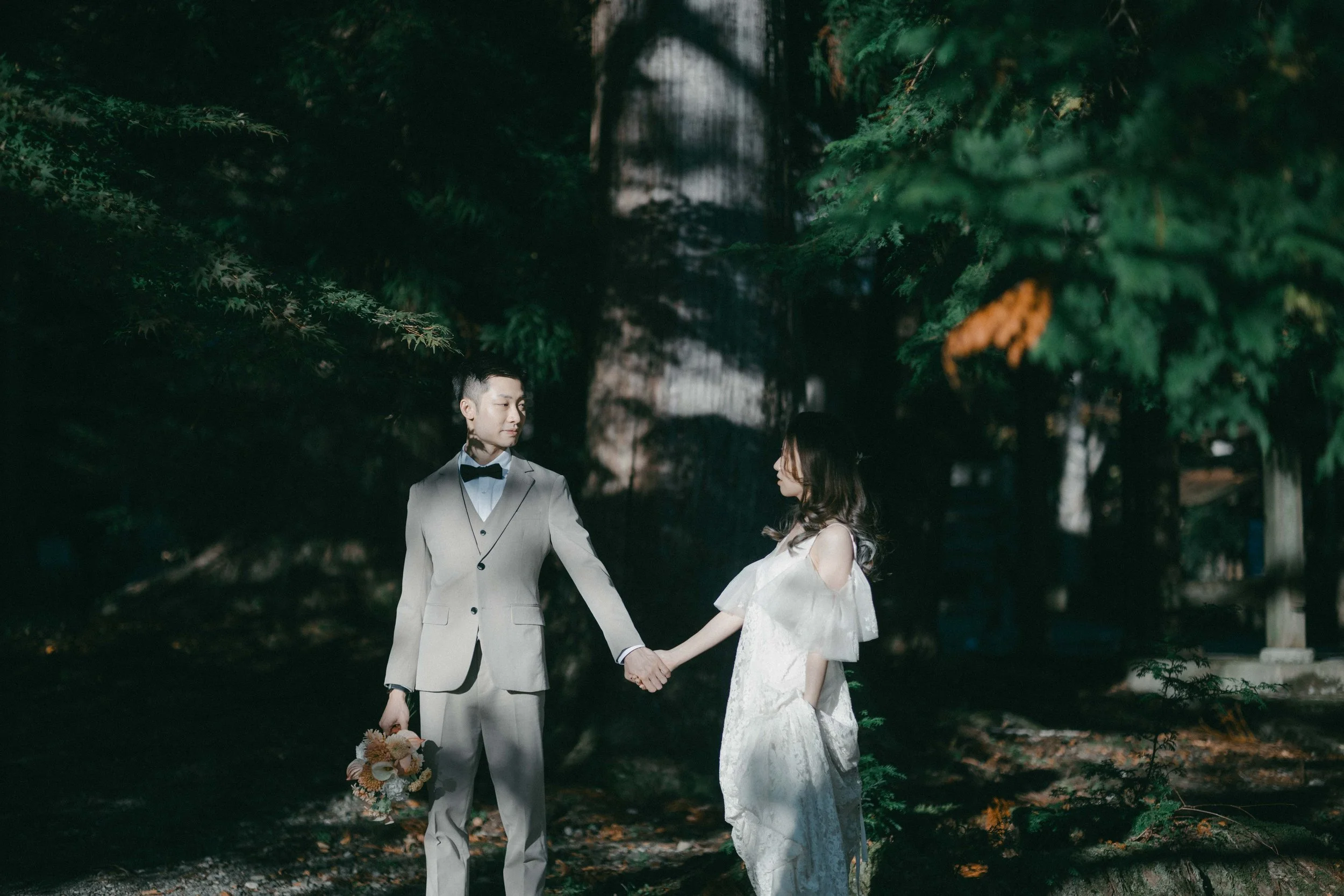 A couple dressed in formal wedding attire holding hands in a forest at night.