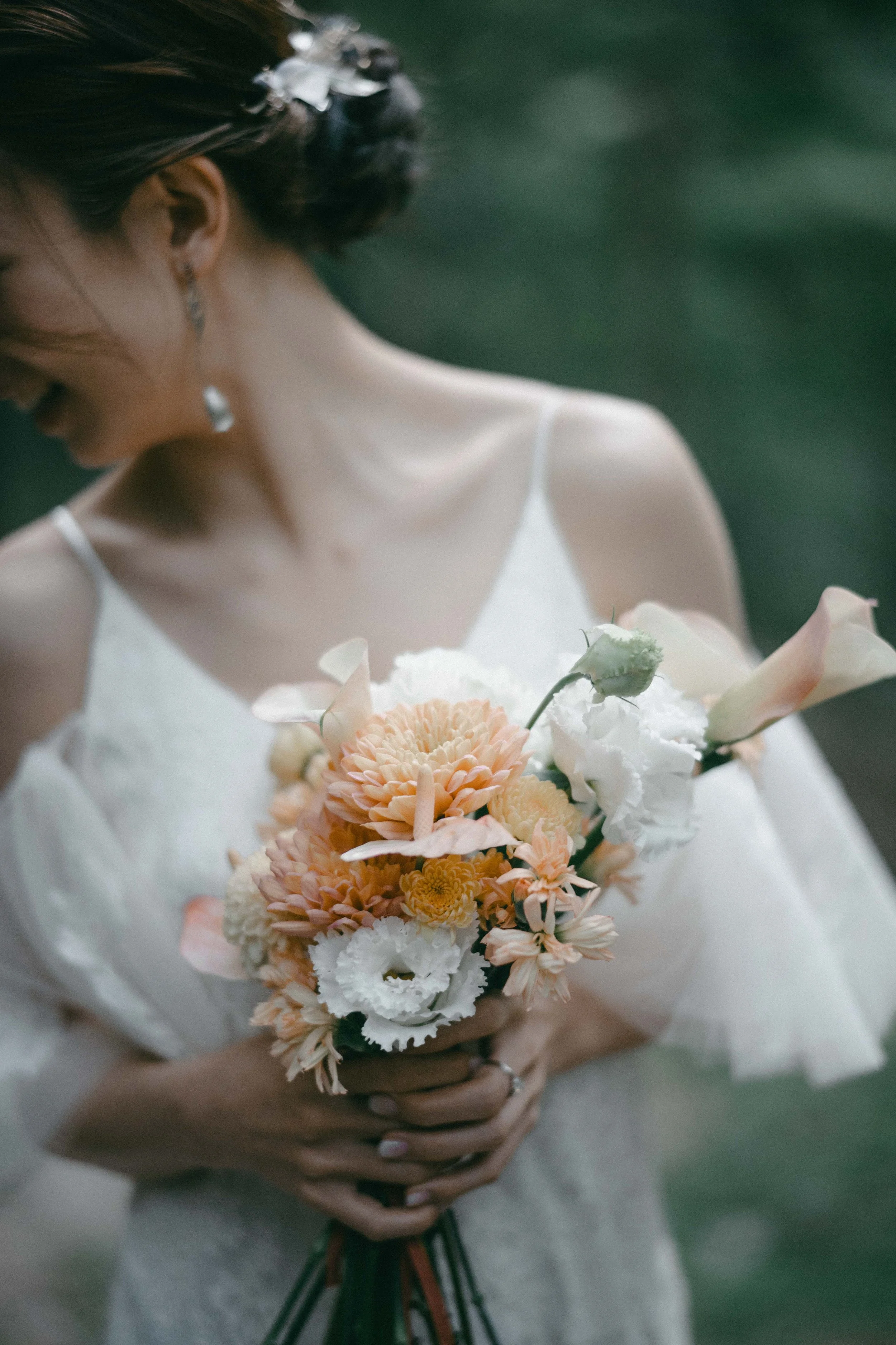 A woman in a white dress holding a bouquet of peach, white, and cream-colored flowers, with a green blurred background.