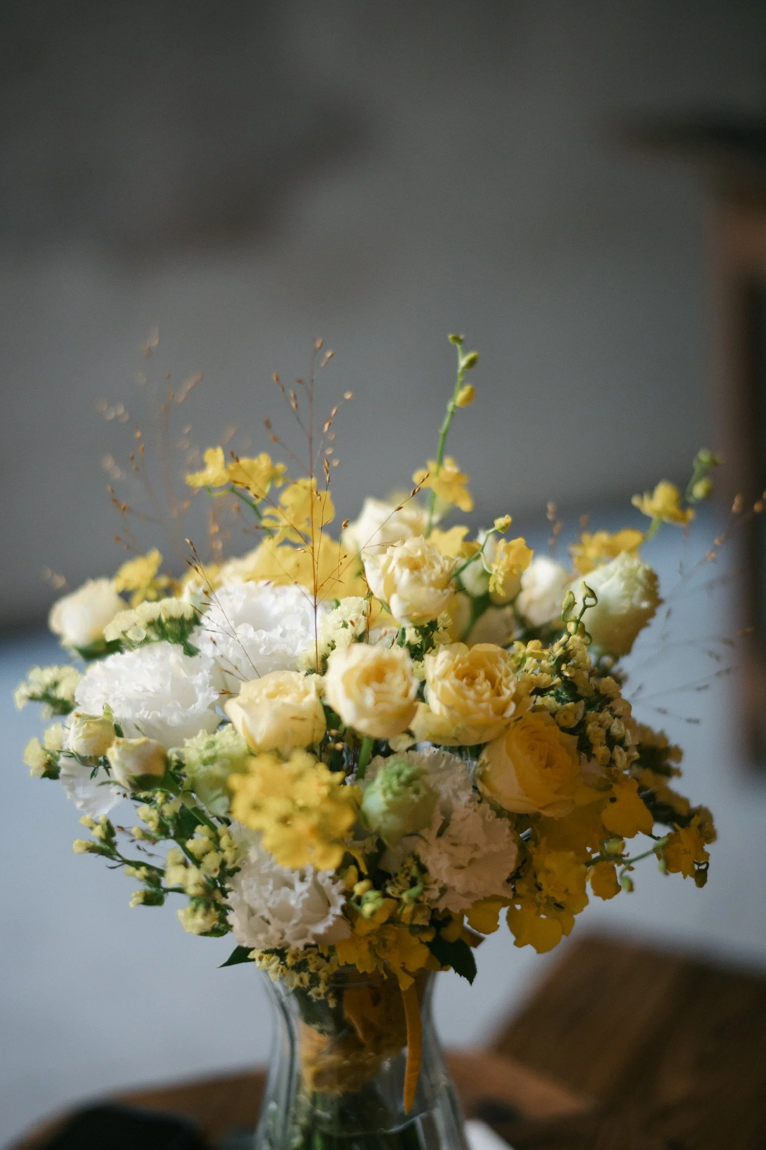 A bouquet of yellow and white flowers in a glass vase on a wooden surface.