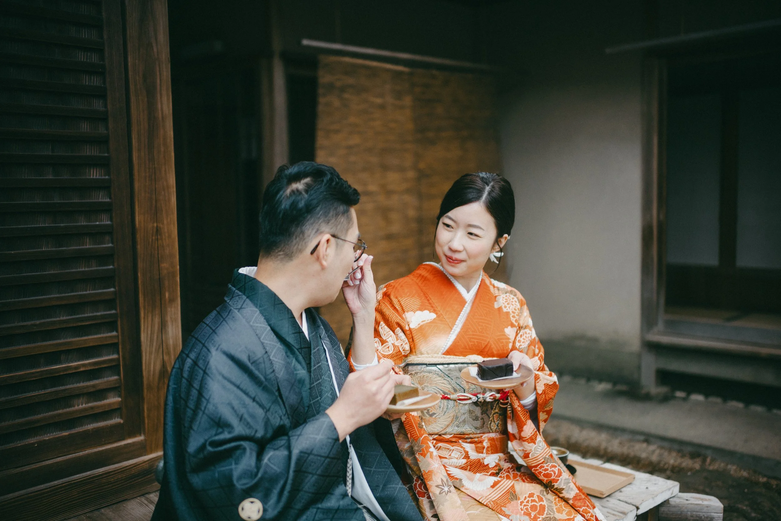 A man and a woman dressed in traditional Japanese kimonos sitting and chatting while eating desserts in a traditional setting.