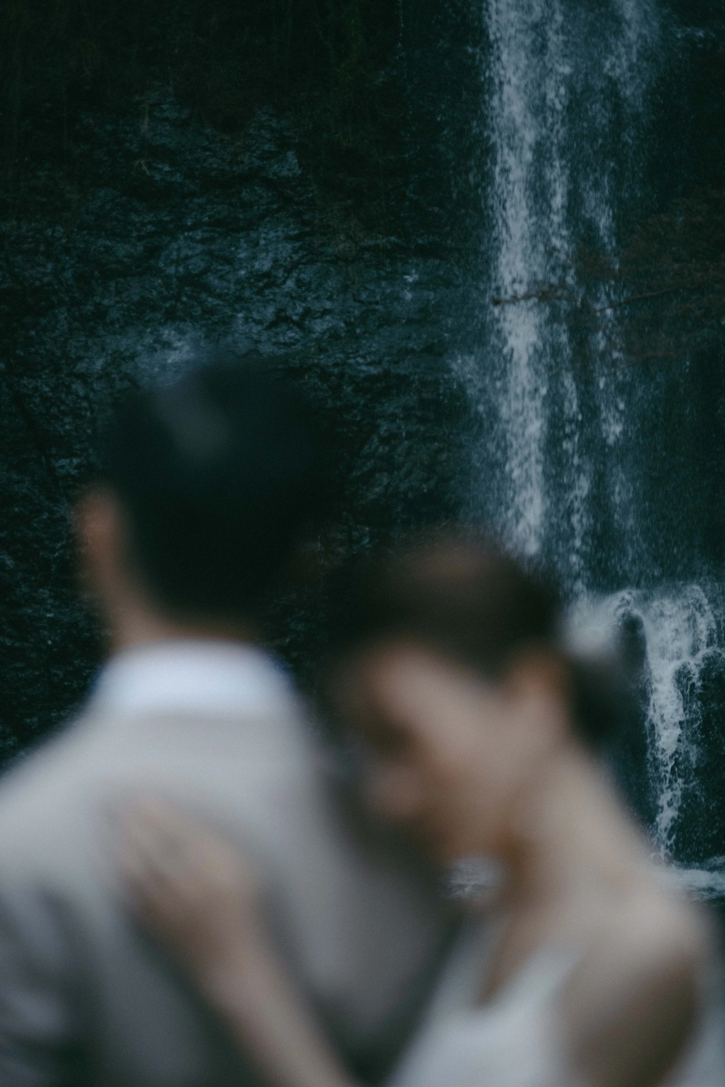 A blurred couple standing in front of a waterfall, with the man in a suit and the woman in a white dress.