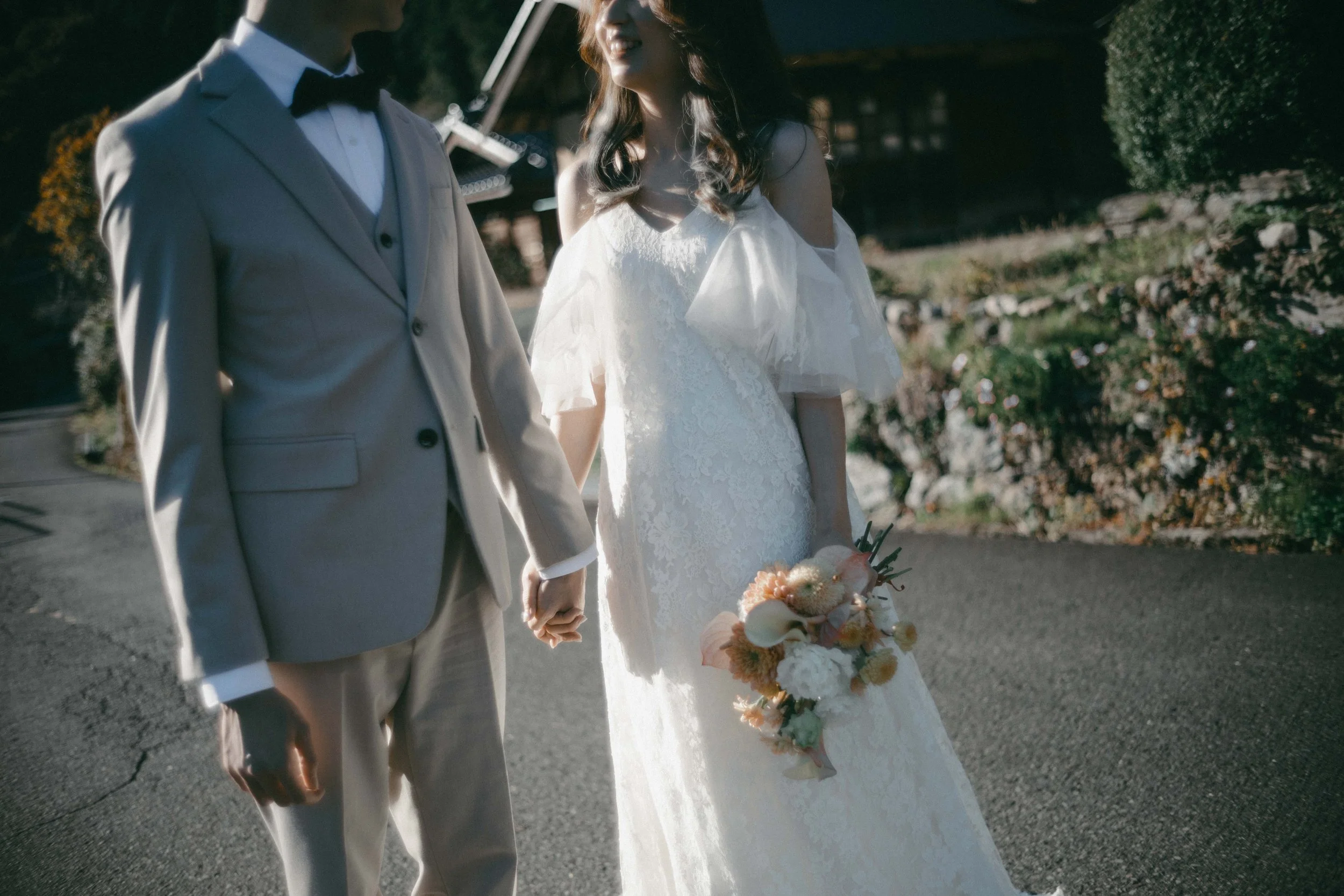 A bride and groom holding hands outdoors before their wedding, with the bride holding a bouquet of flowers.