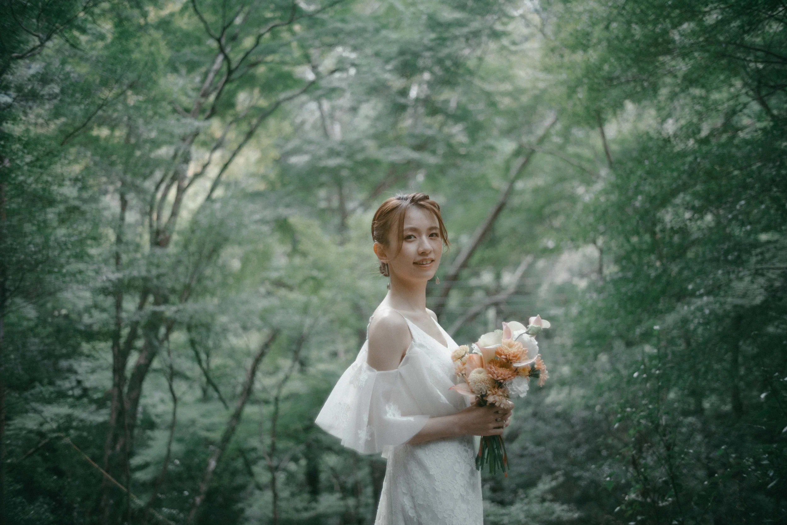 A woman in a white dress holding a bouquet of flowers in a lush green forest.