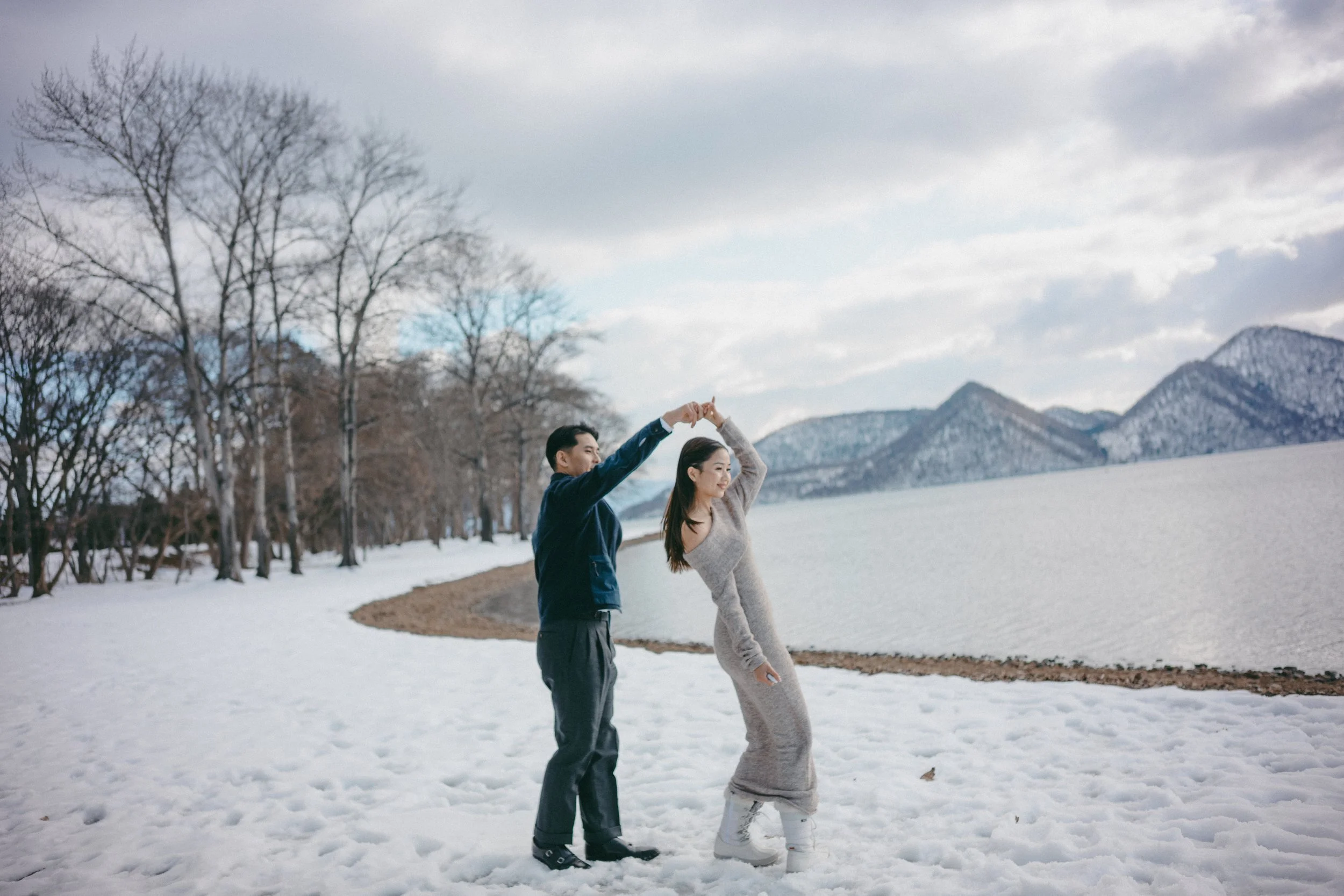 A couple dancing in the snow by a lake with mountains in the background.