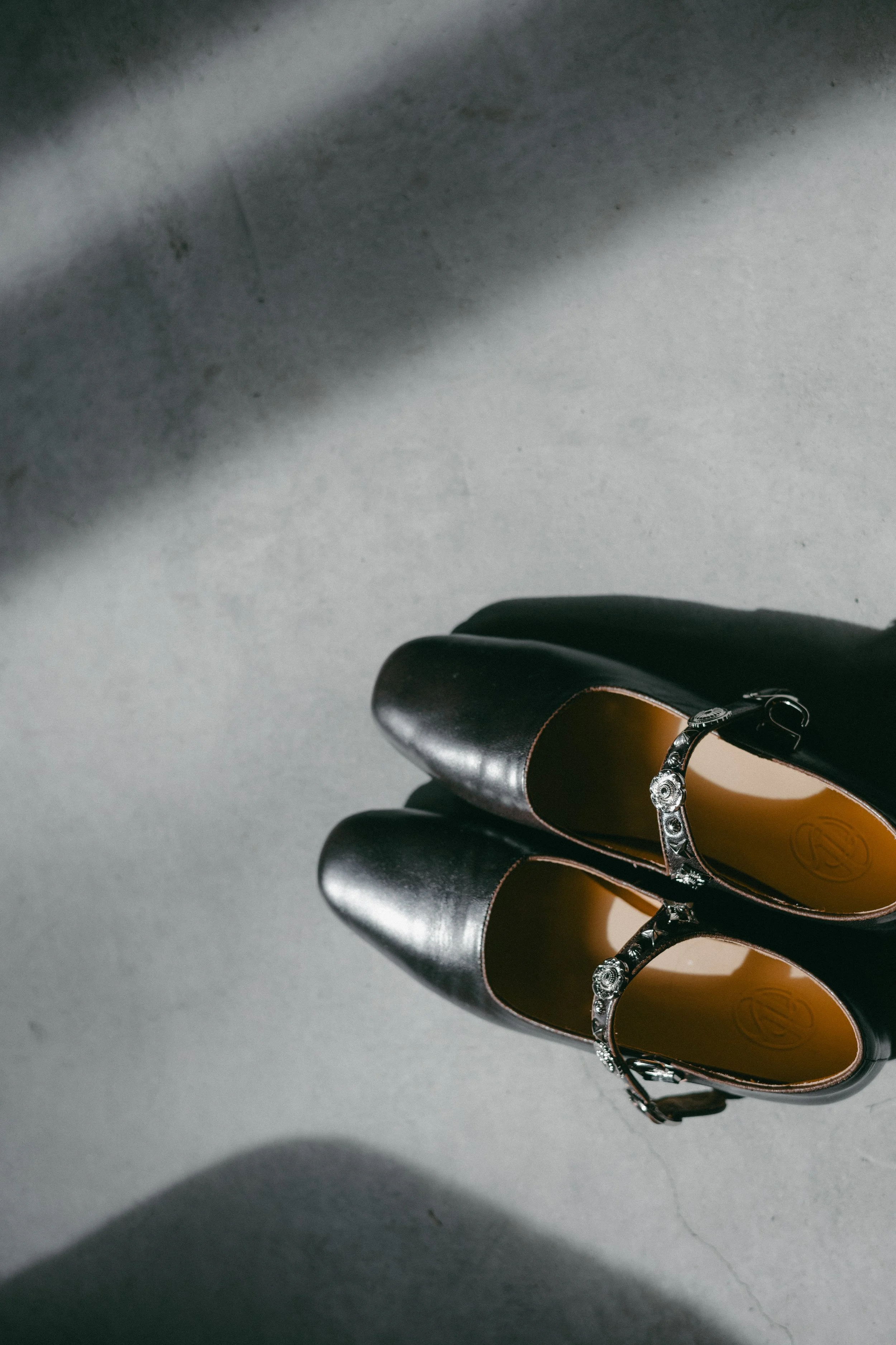 A pair of black women's Mary Jane shoes with ankle straps and decorative embellishments, placed on a gray surface with shadows.
