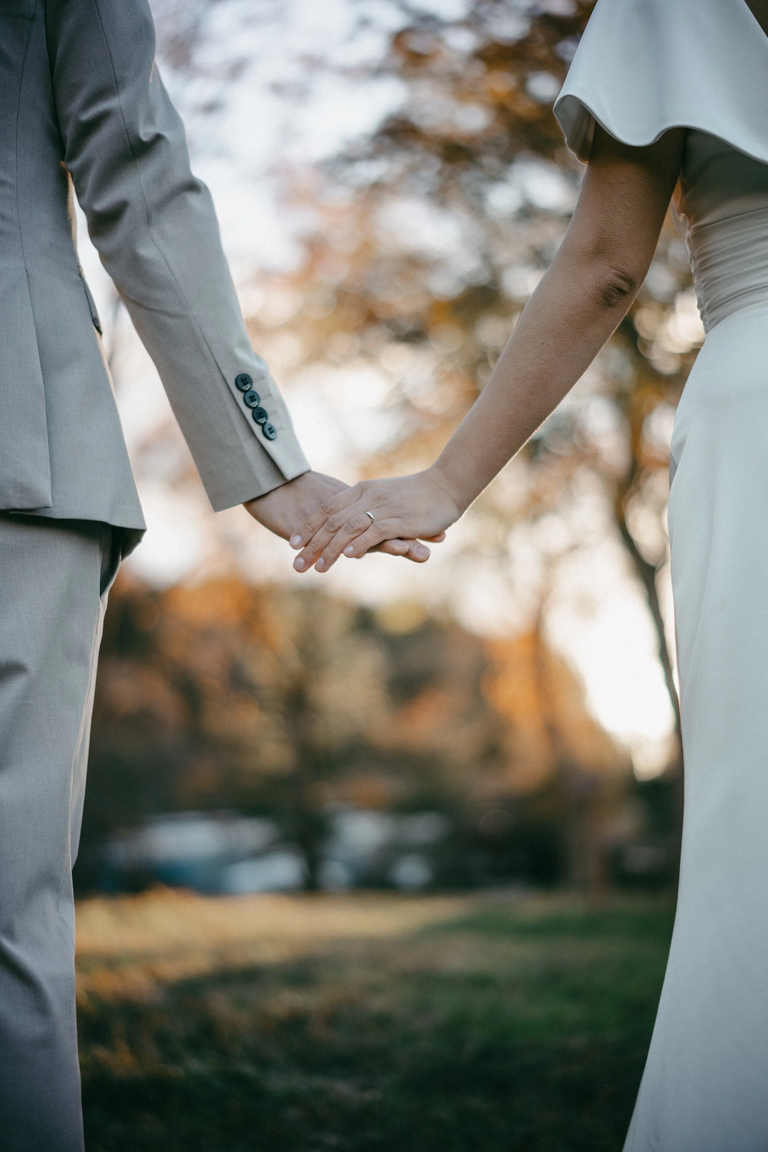 A couple holding hands outdoors during sunset, with trees and blurred background.