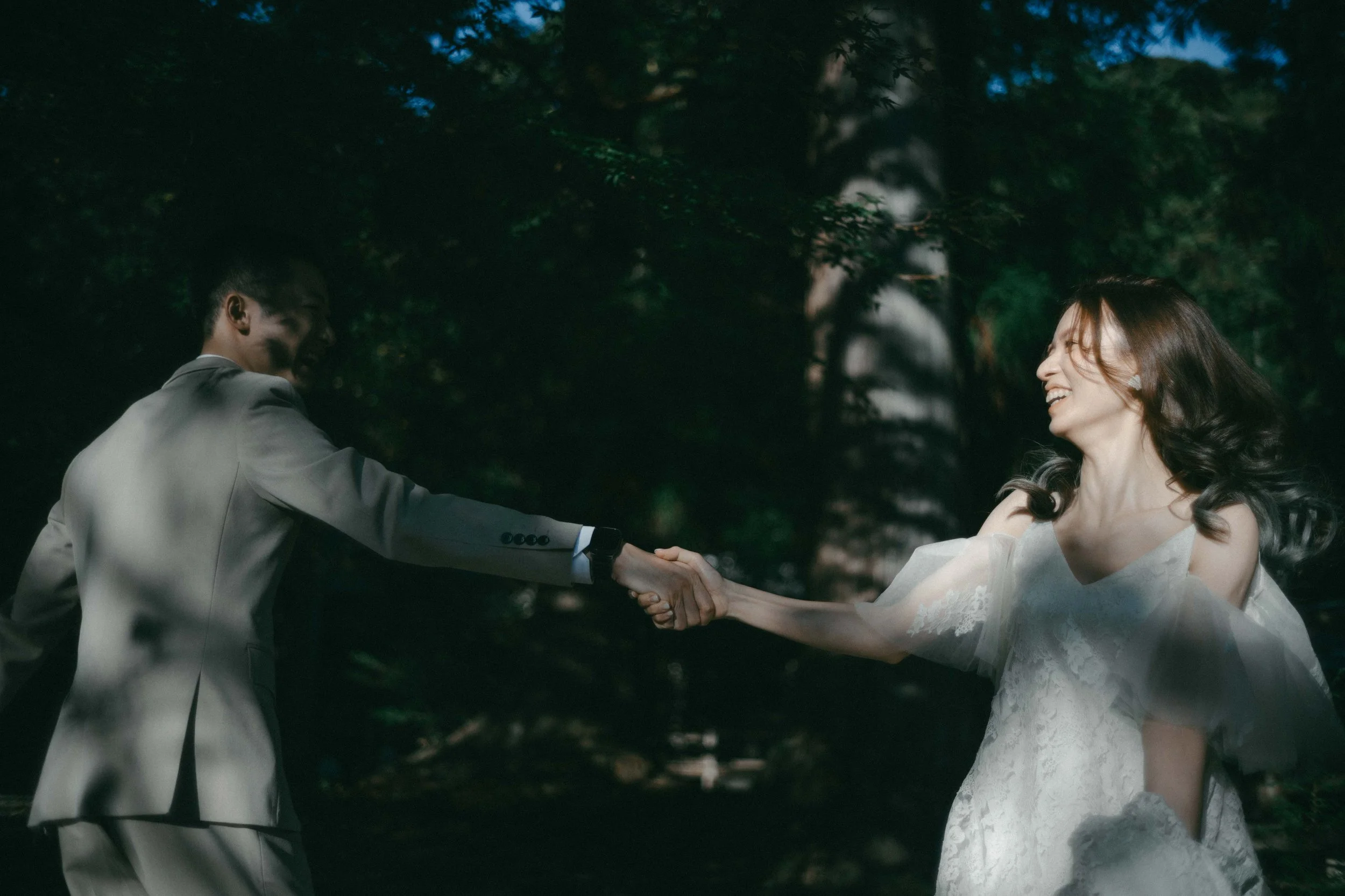 A couple in wedding attire holding hands and smiling in a forest setting.