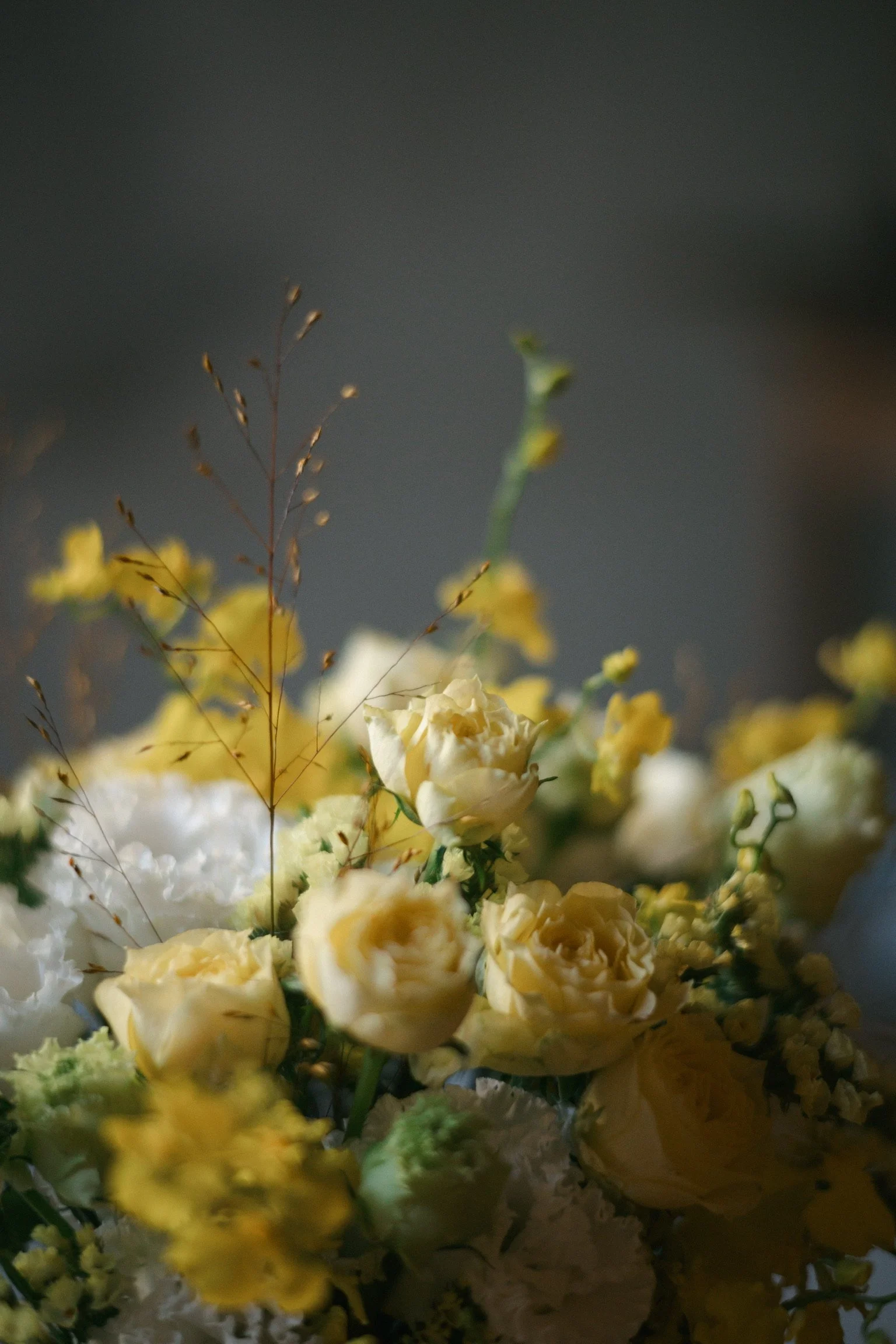 Close-up of a soft yellow and white flower bouquet with greenery and delicate branches on a blurred background.