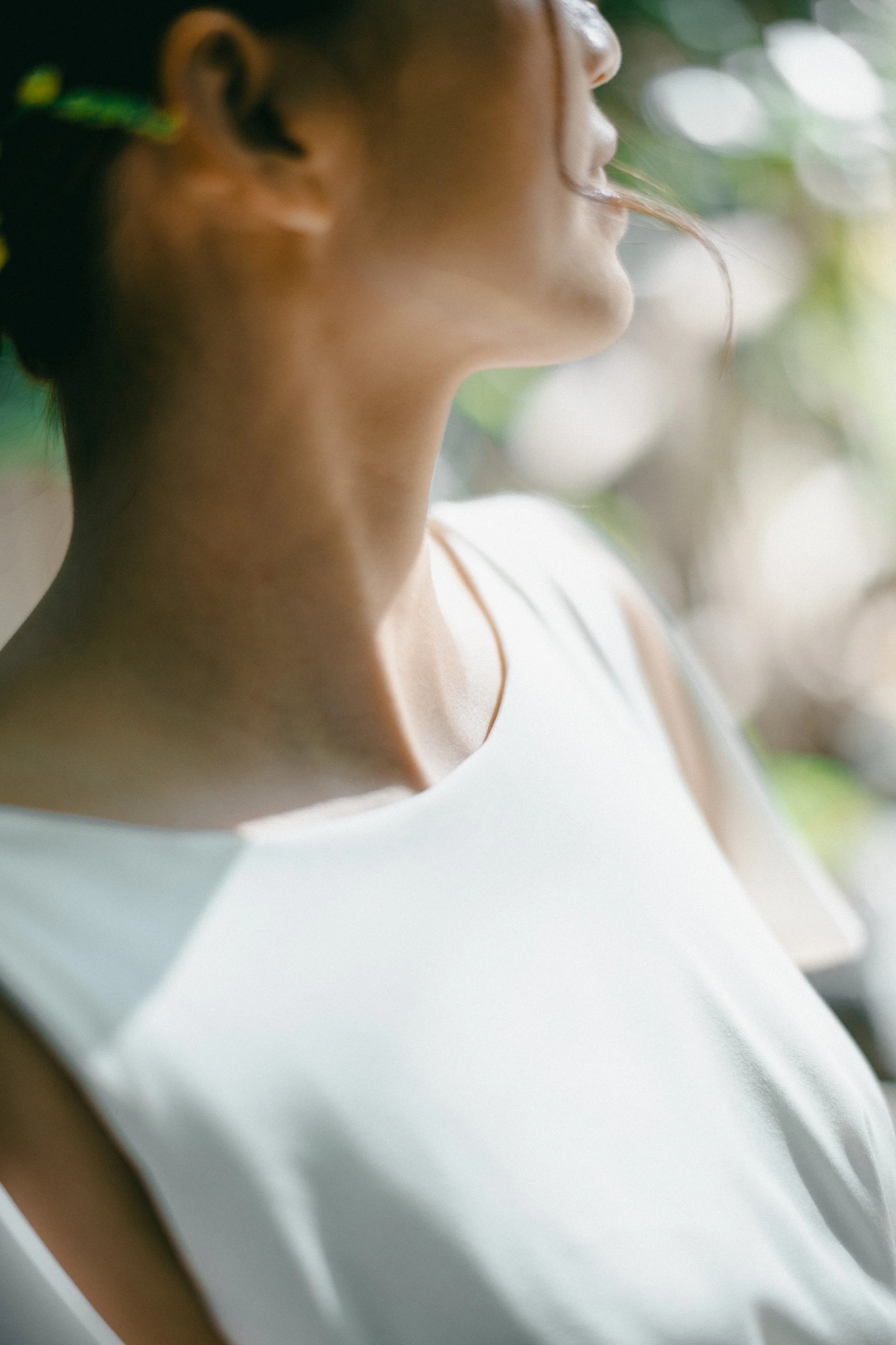 Close-up of a woman in a white top, emphasizing her neck and jawline, with her face partly visible in profile, set against a blurred background.