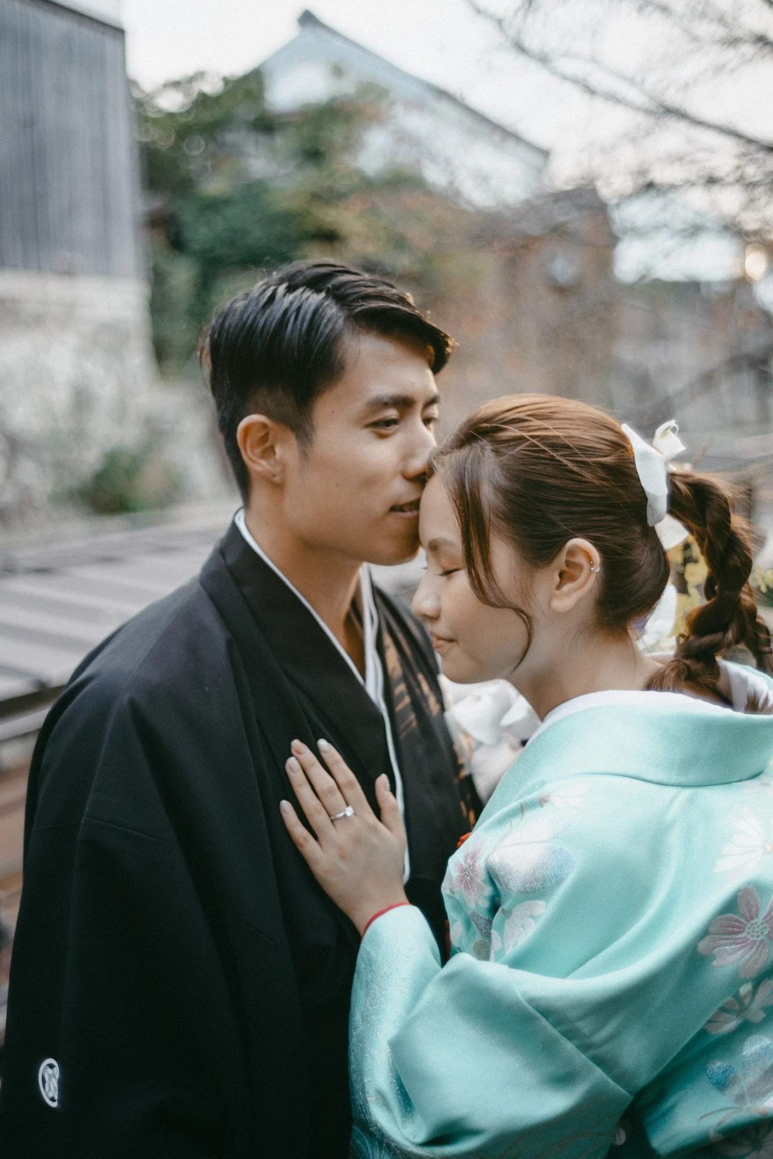A couple sharing an intimate moment outdoors, with the man gently touching the woman's forehead, both appearing emotional and close to each other.
