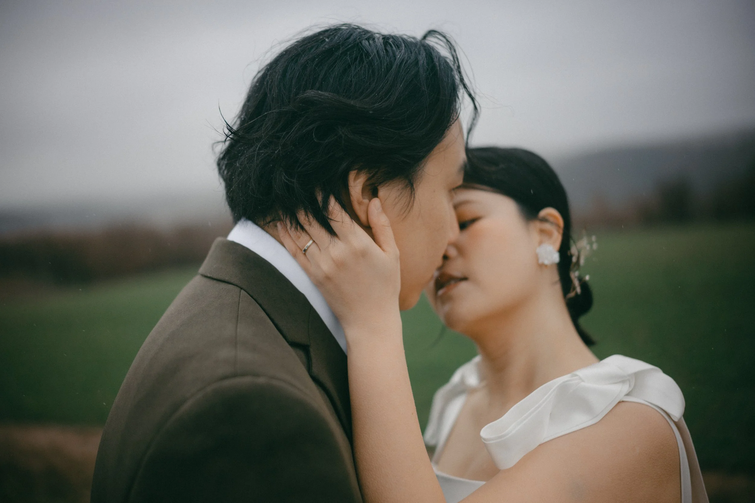 A romantic moment shows a couple kissing outdoors, with the woman's hand gently touching the man's face, both dressed elegantly.