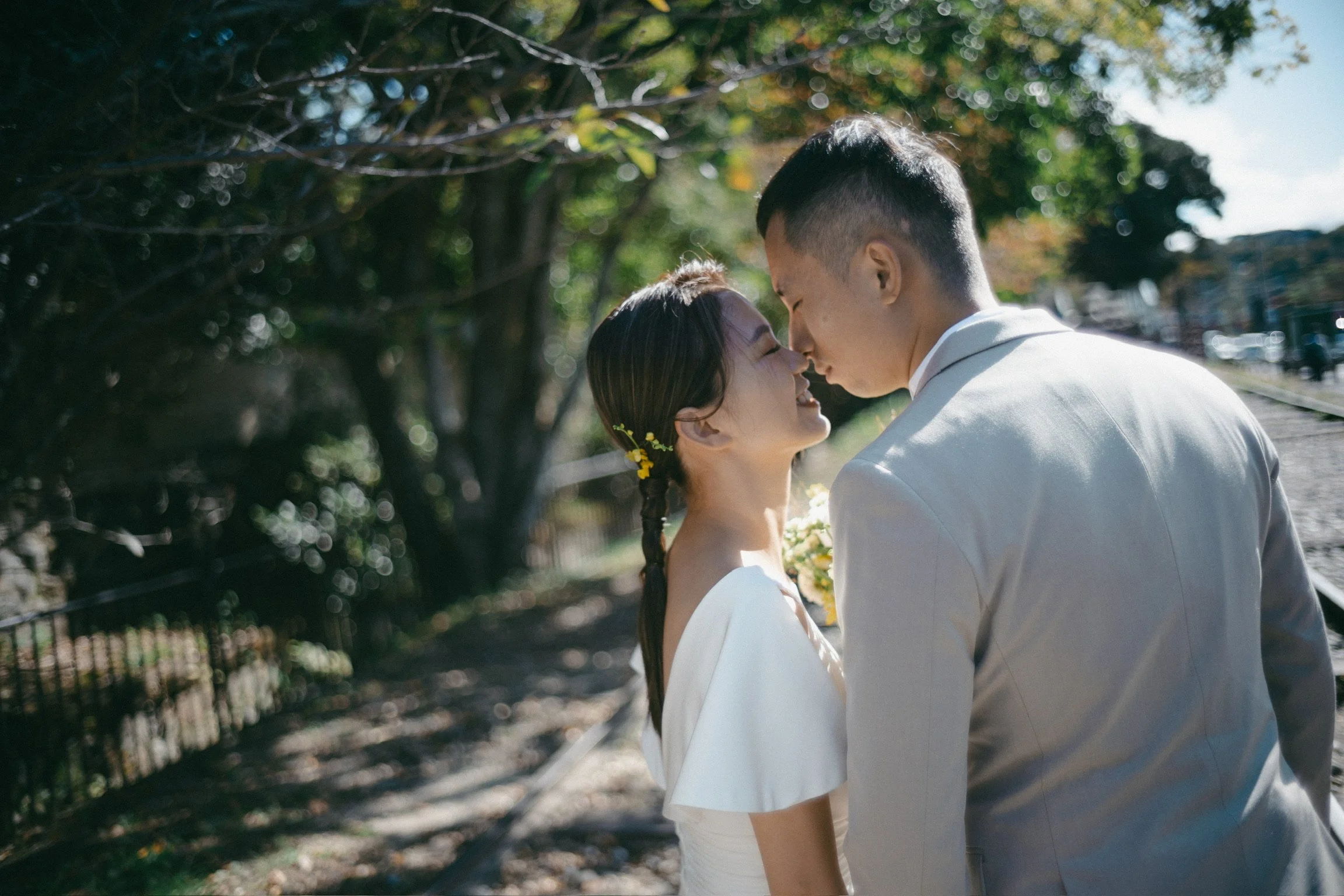 A couple in wedding attire sharing an intimate moment, forehead to forehead, on train tracks surrounded by trees and natural light.
