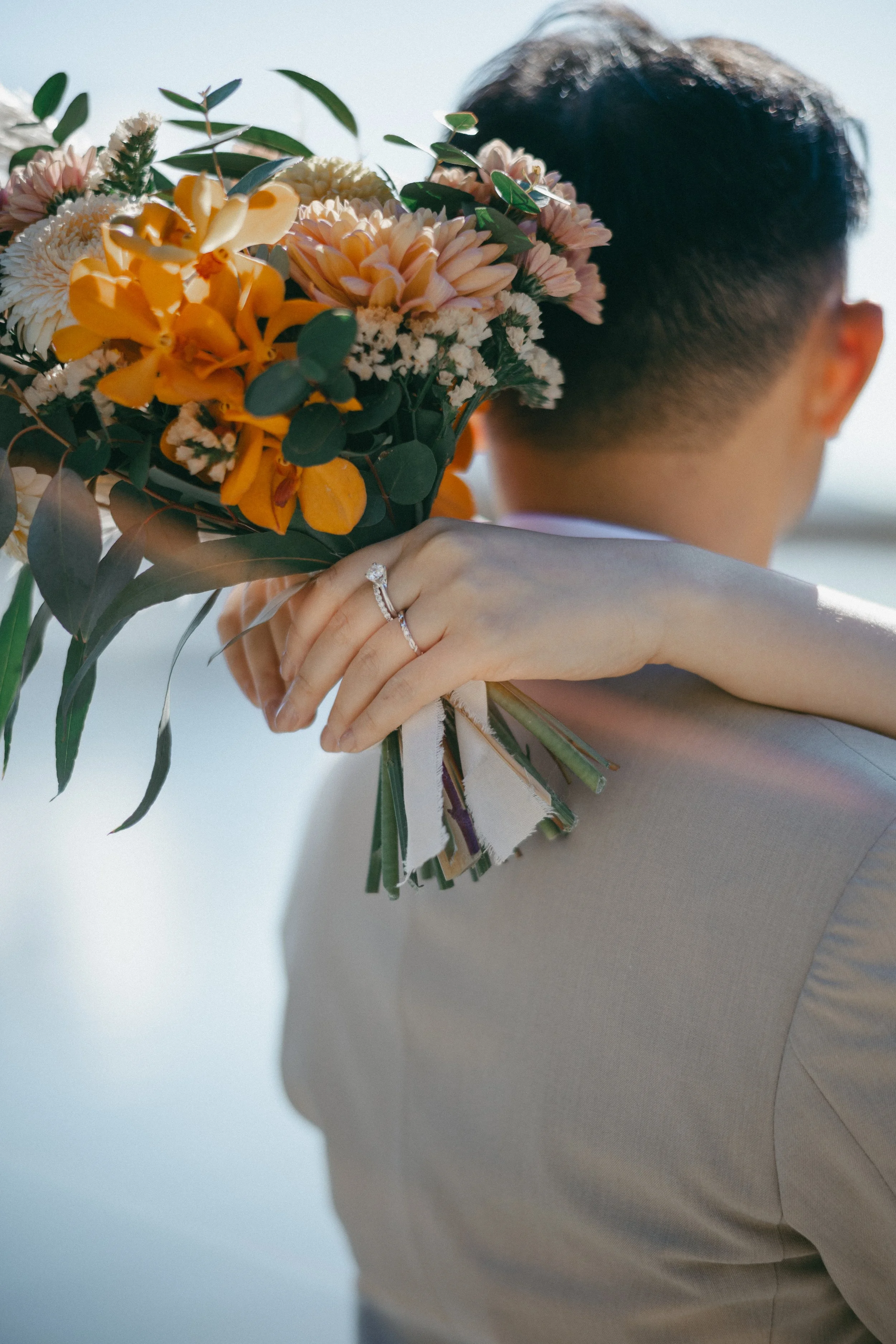 Person holding a bouquet of flowers over their shoulder, wearing a ring on their finger.