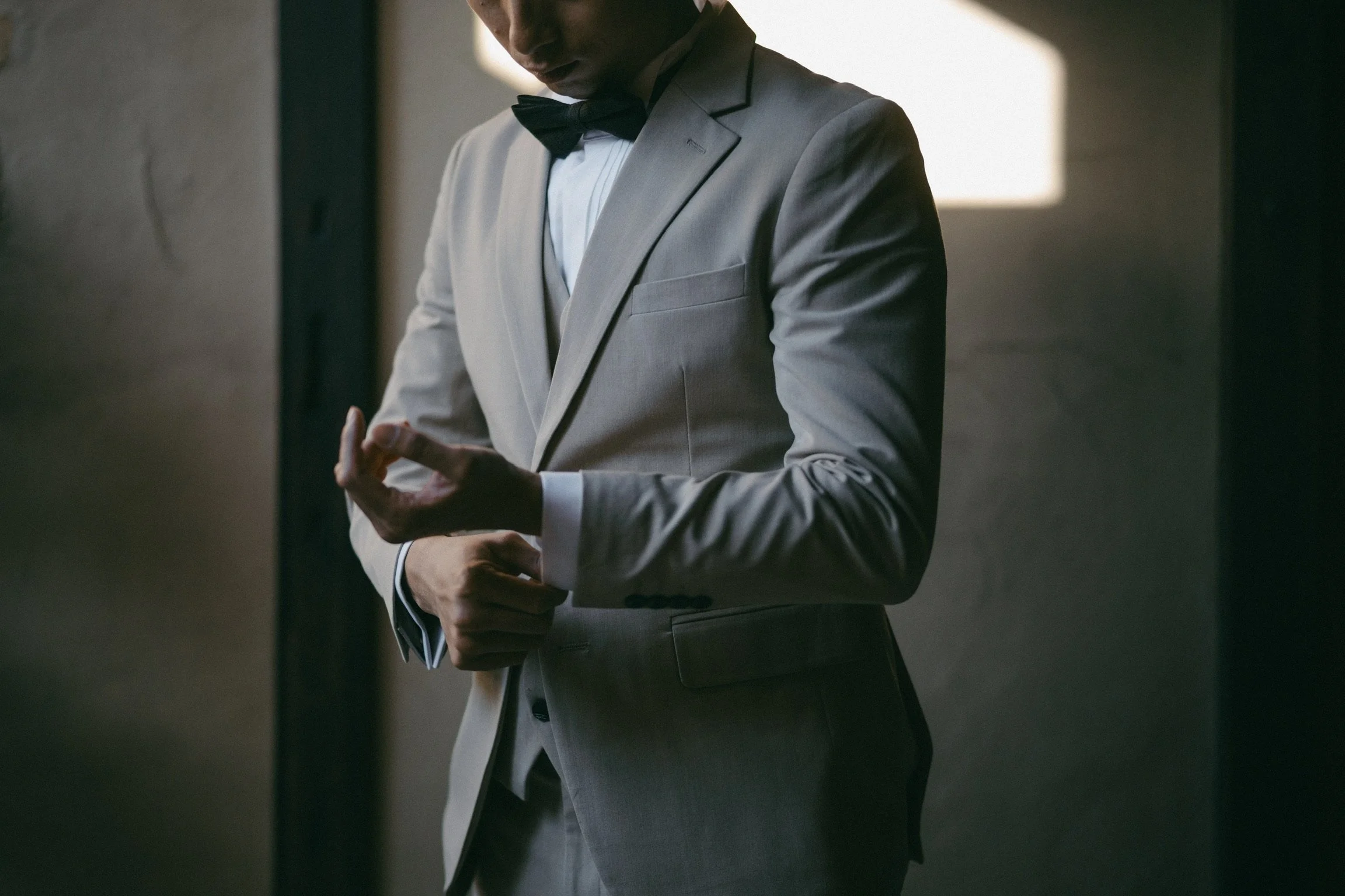 Man in a light grey suit adjusting his cuff links.