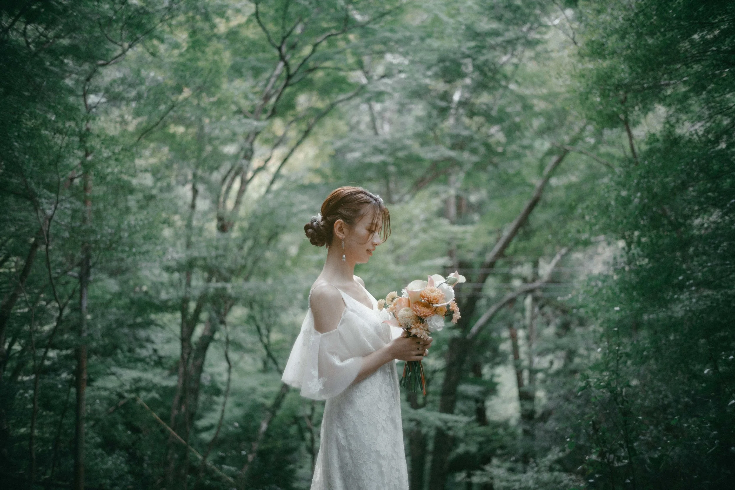 A woman in a white dress holding a bouquet of flowers, standing in a lush green forest.