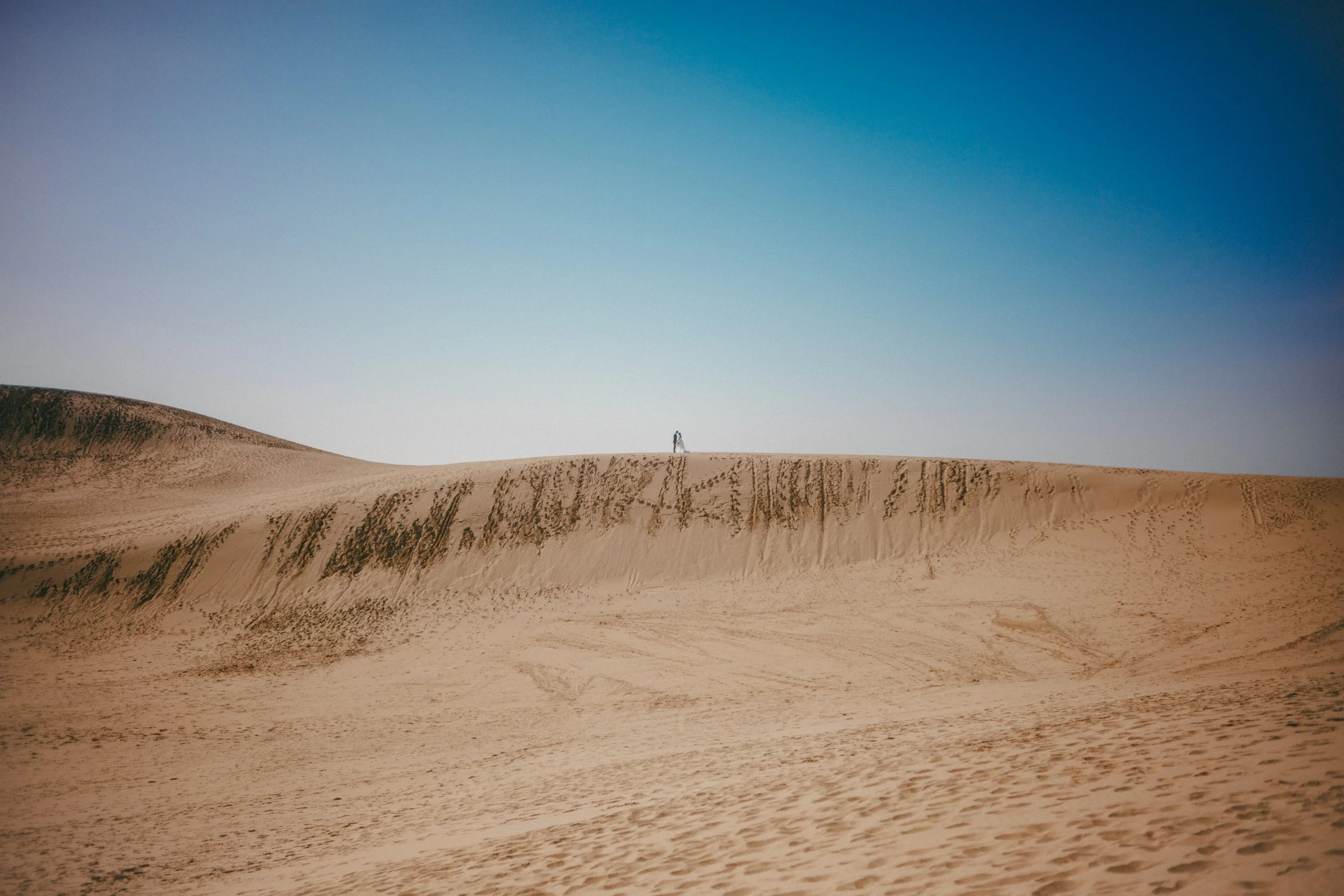 Person standing on top of sand dunes in a desert landscape with a clear blue sky.