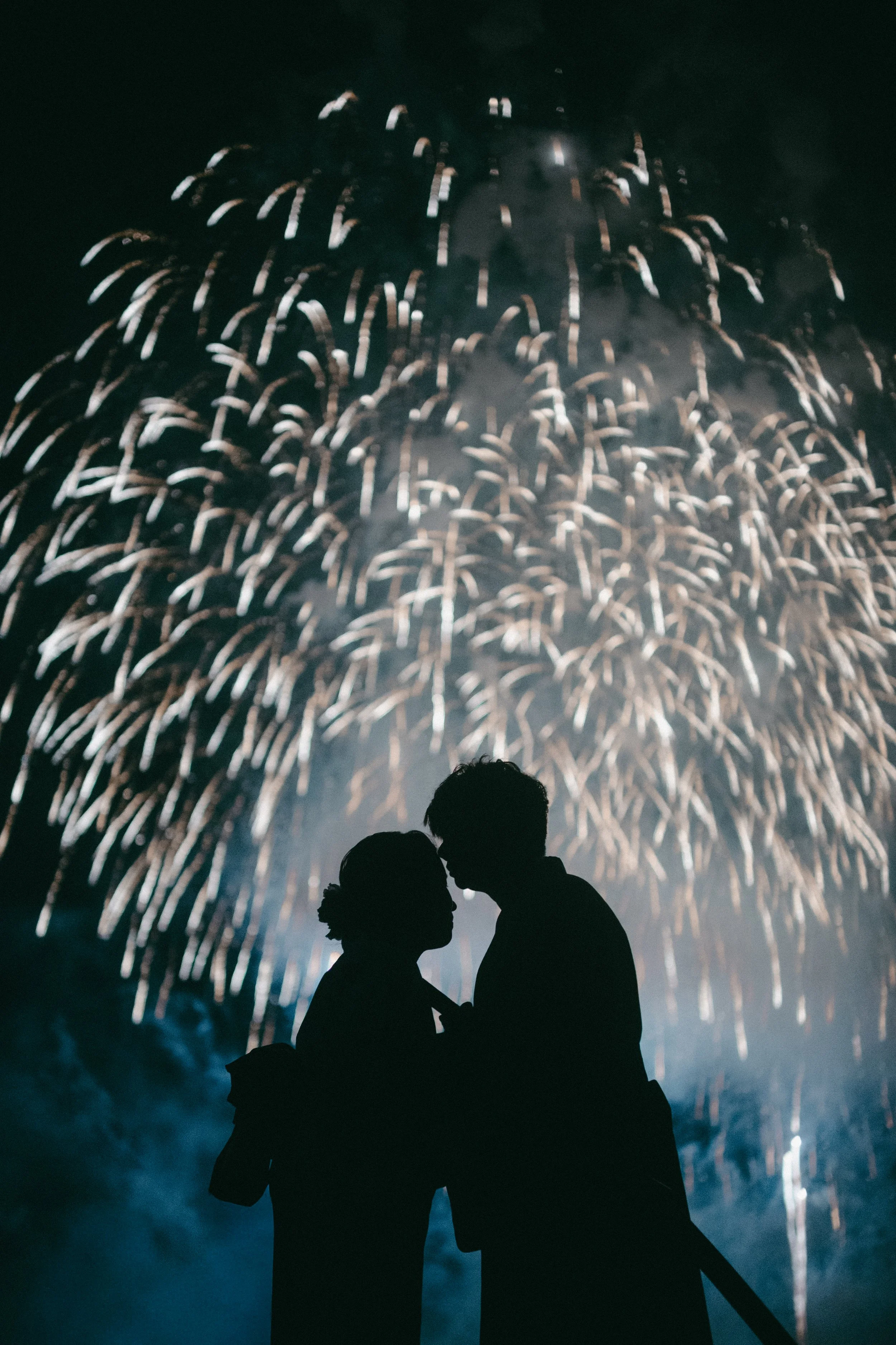 Silhouettes of a couple in a close embrace during fireworks celebration at night.