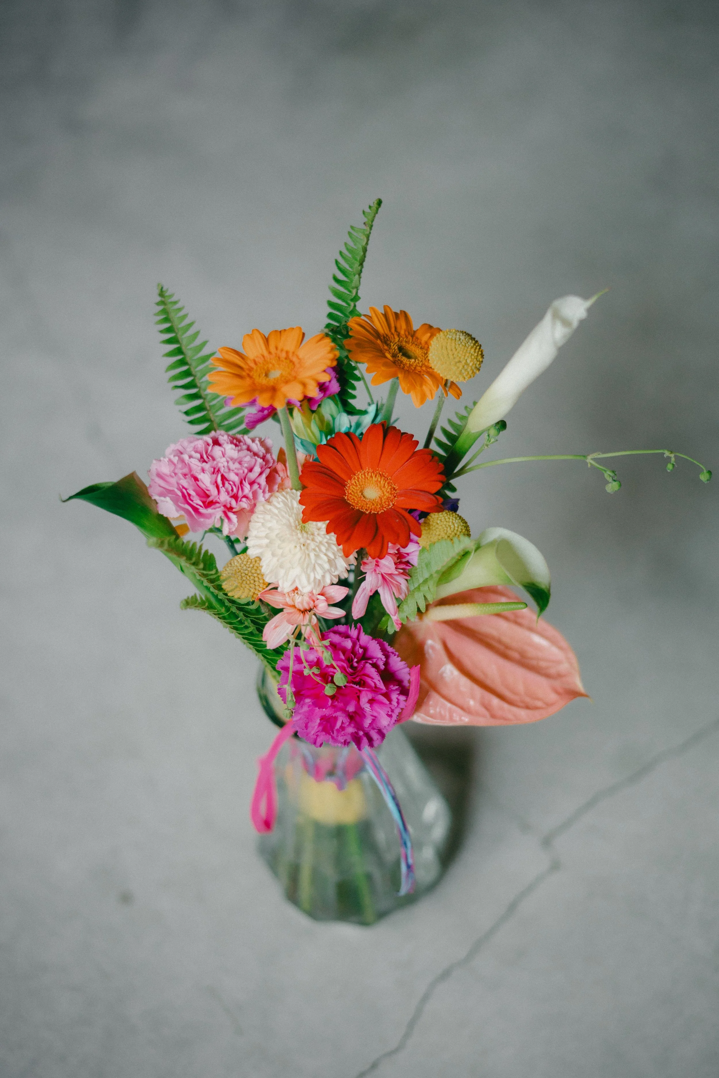 A colorful bouquet of flowers in a small glass vase, placed on a gray surface.