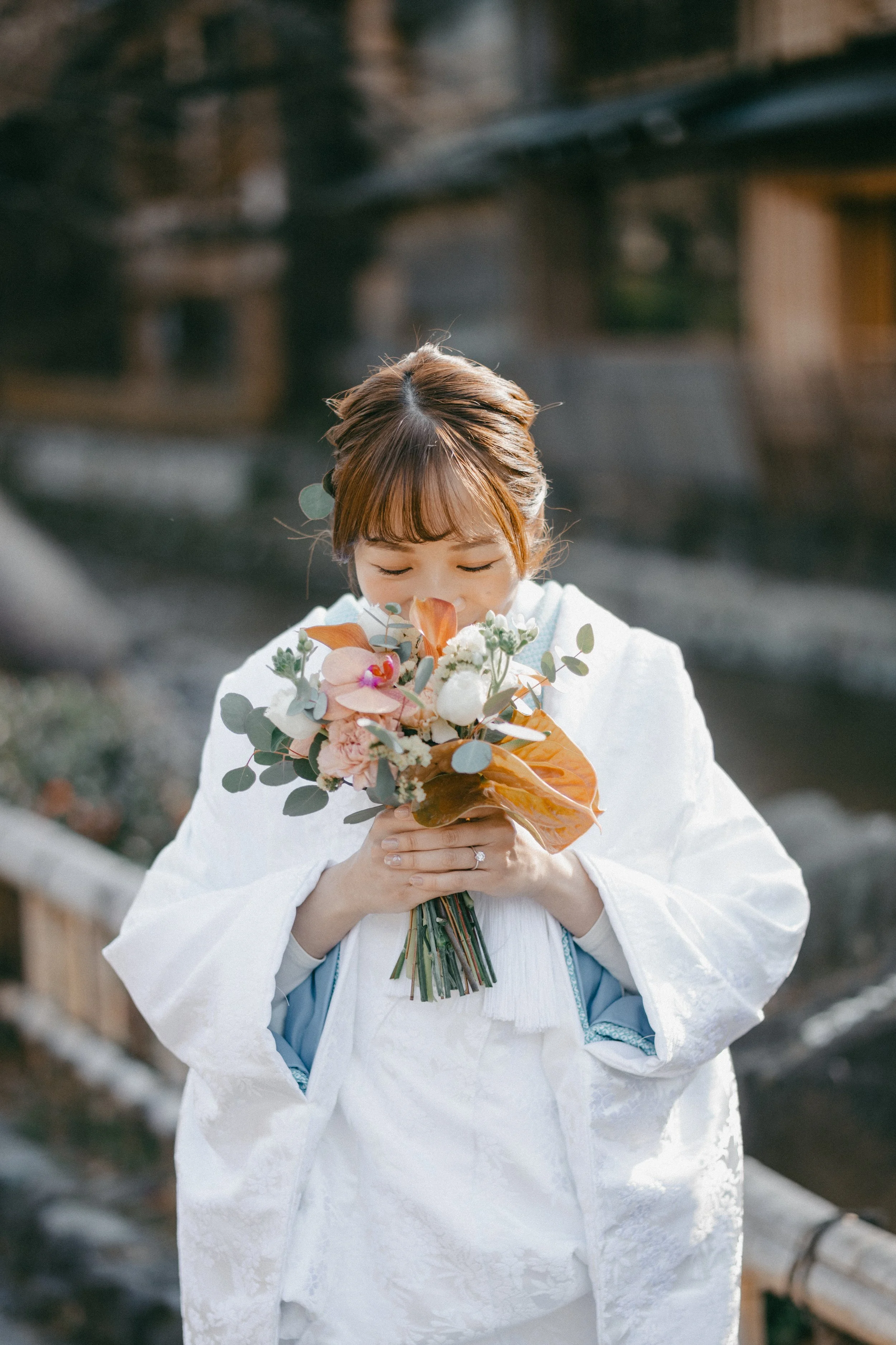 A woman dressed in traditional white attire holding a bouquet of flowers close to her face outdoors.