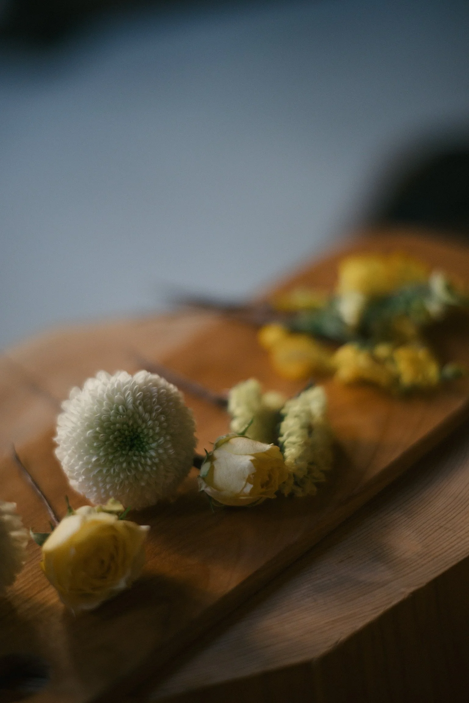 Dried flowers including a white globe-shaped flower and yellow roses arranged on a wooden surface.