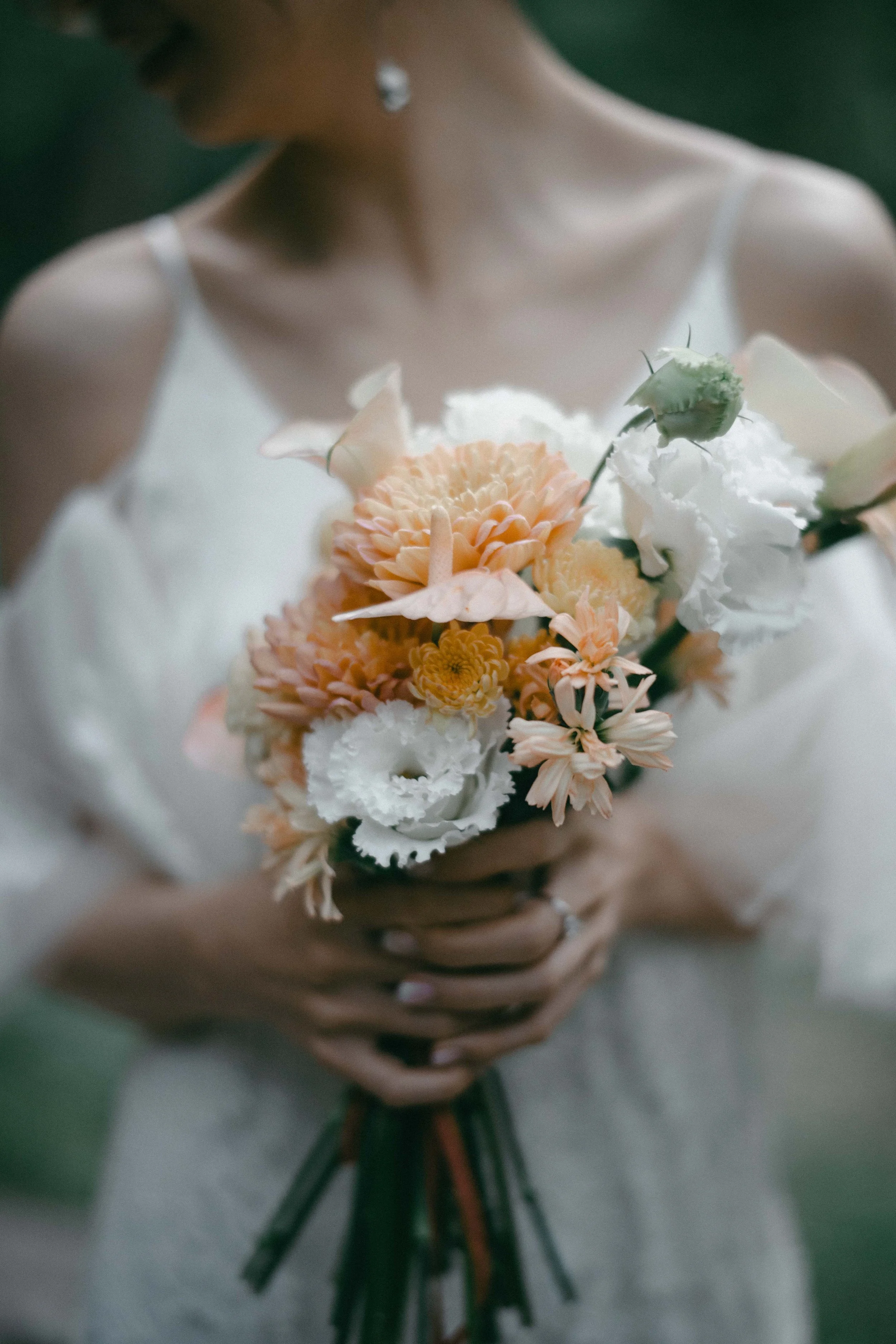 A woman in a white dress holding a bouquet of light peach and white flowers.