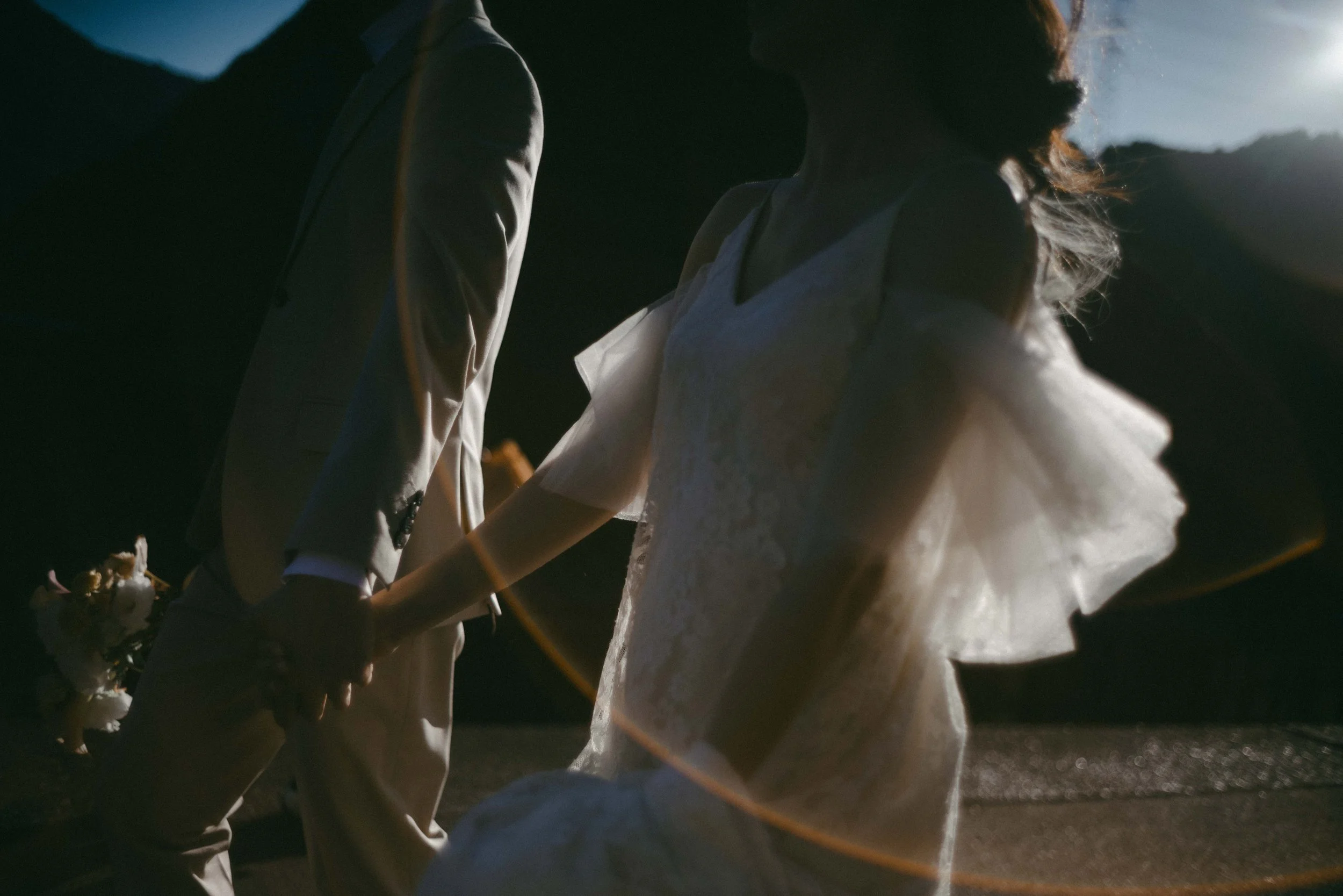 A couple holding hands during a wedding at sunset, with mountains in the background.