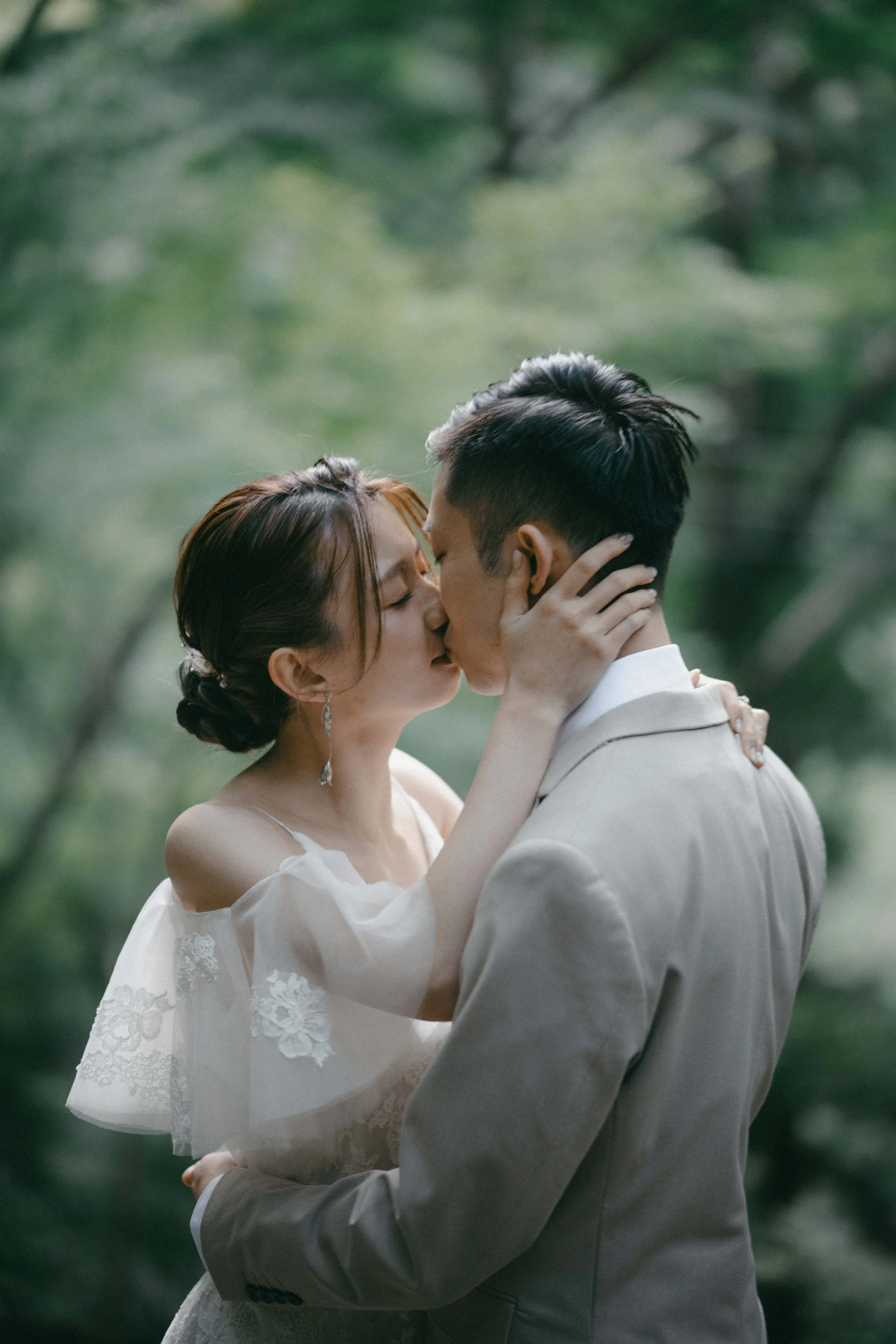 A couple shares a kiss in a lush, green outdoor setting, with the woman holding the man's face and the man holding her waist.