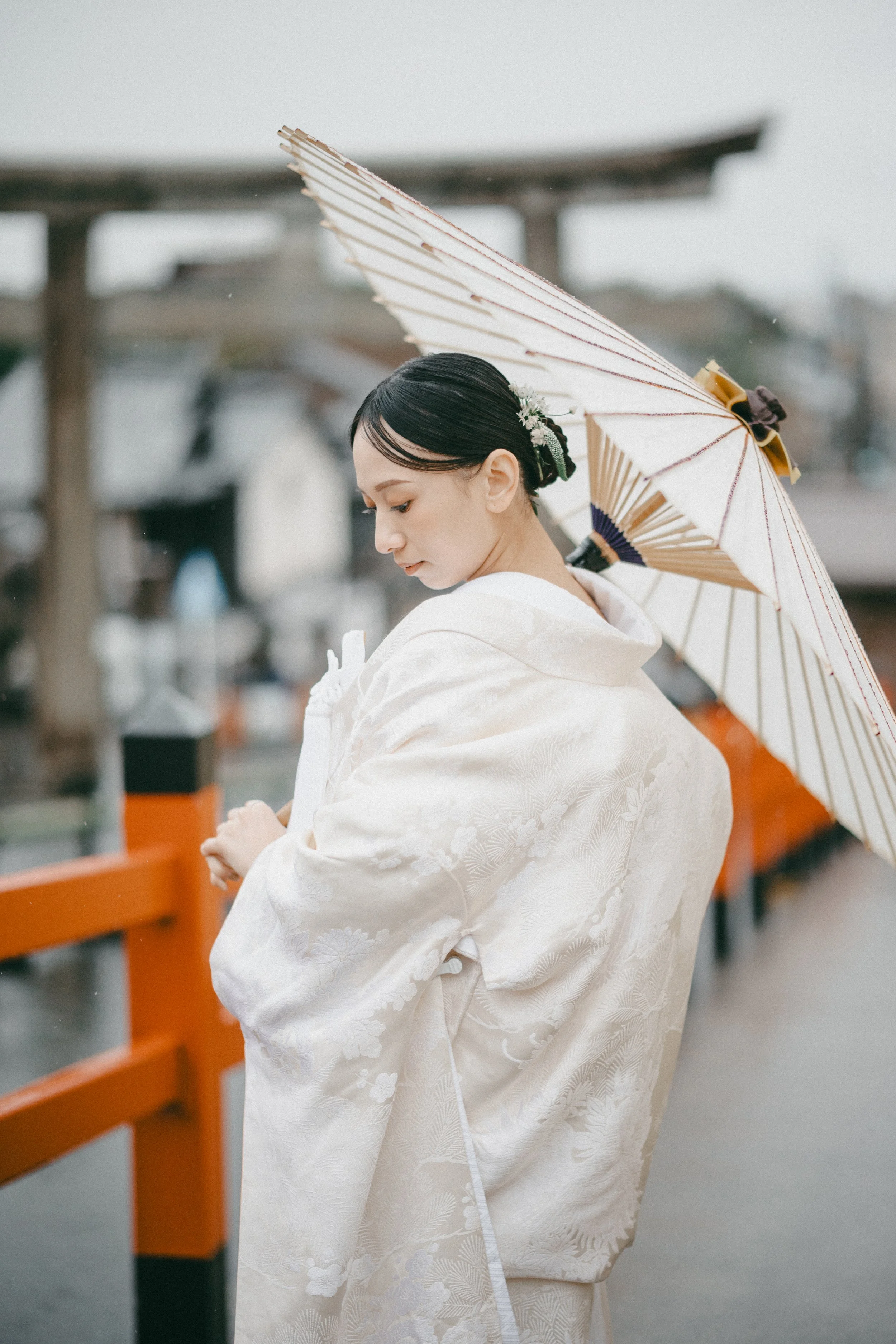 A young woman in traditional Japanese wedding attire holding an umbrella, standing on a bridge.